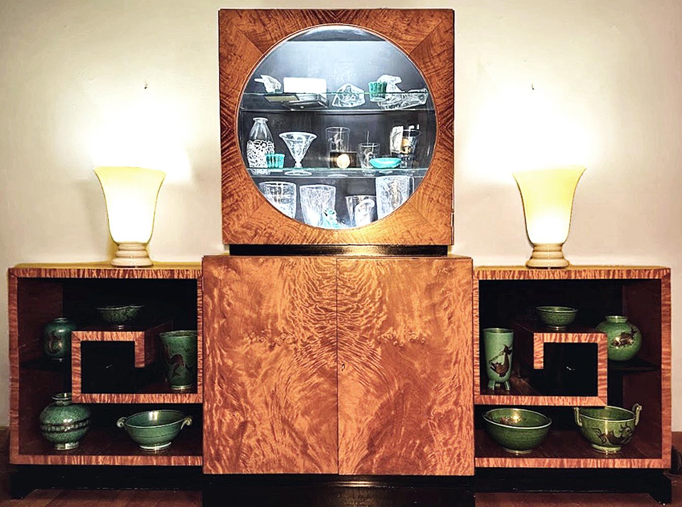 Stunning in concept and execution, this large, impressive Moderne-Art Deco cabinet consists of four parts, all centered around an internally-lit porthole vitrine with glass shelves and convex bubble window, all finished in a golden flame mahogany