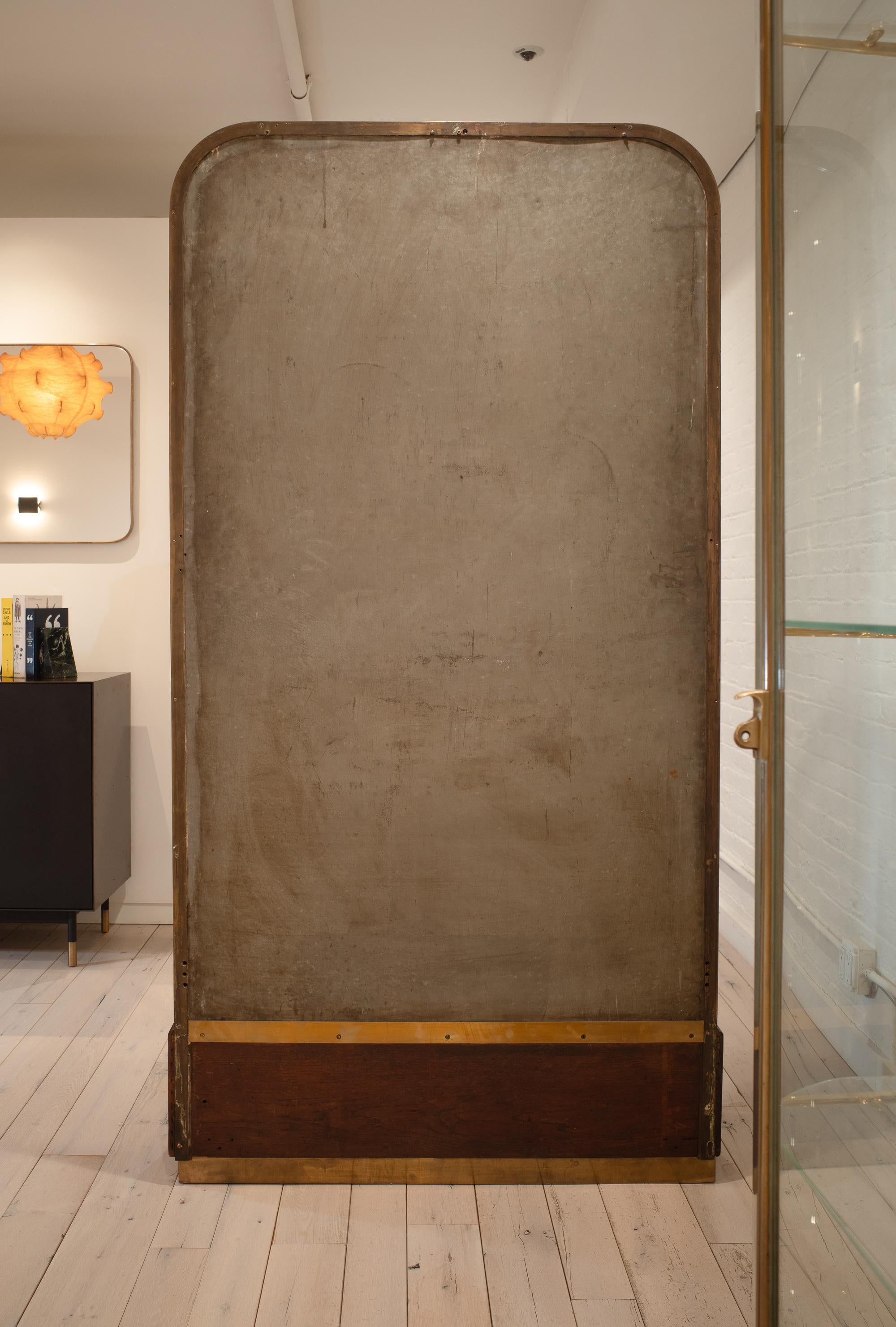 This art deco era display cabinet, circa 1930, was made in Paris by LENA at 160 Rue Oberkampf. Constructed from brass and mahogany, it features a large glass door that opens to reveal adjustable glass shelves with brass supports and a mirrored