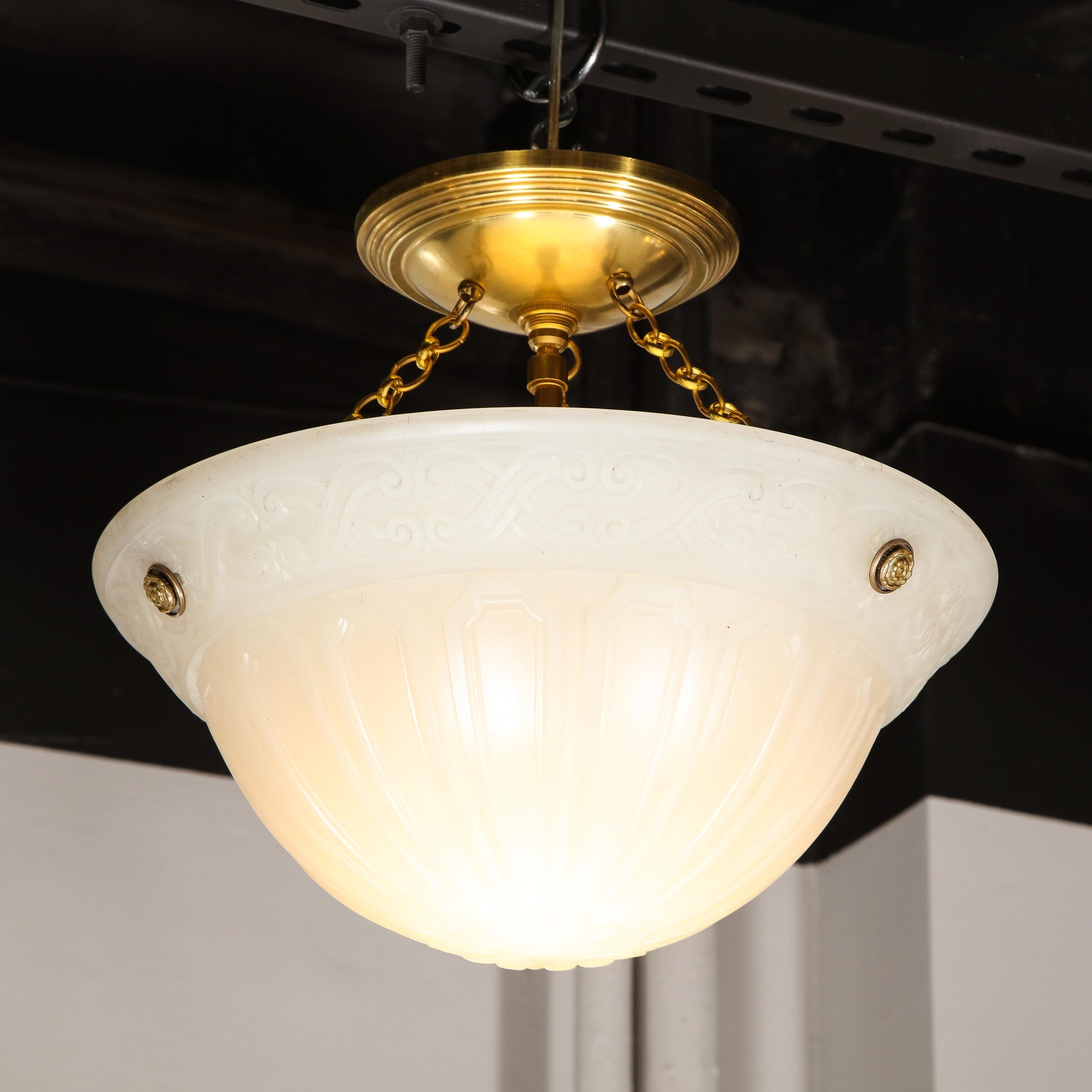This elegant Art Deco pendant was realized in the United States circa 1930. it features a domed milk glass body replete with a geometric arch form detailing around its domed body; starburst flame detailing at its nadir; and stylized neoclassical x