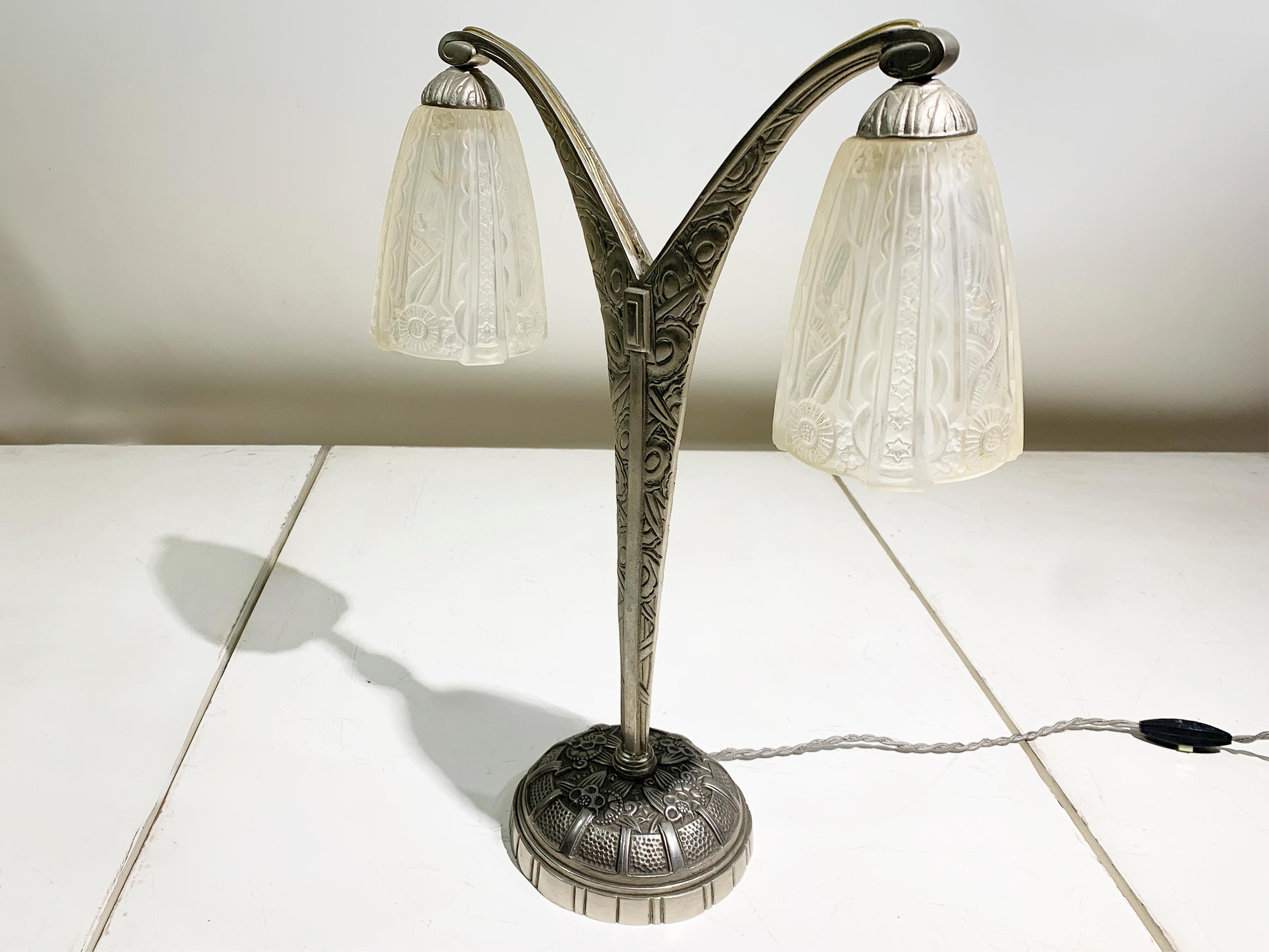 The table lamp features a beautifully sculpted double arm design rising from a streamlined base. The body and arms are crafted from nickeled bronze, which provides a substantial feel and classic patinated finish. 

The true showpieces of this lamp