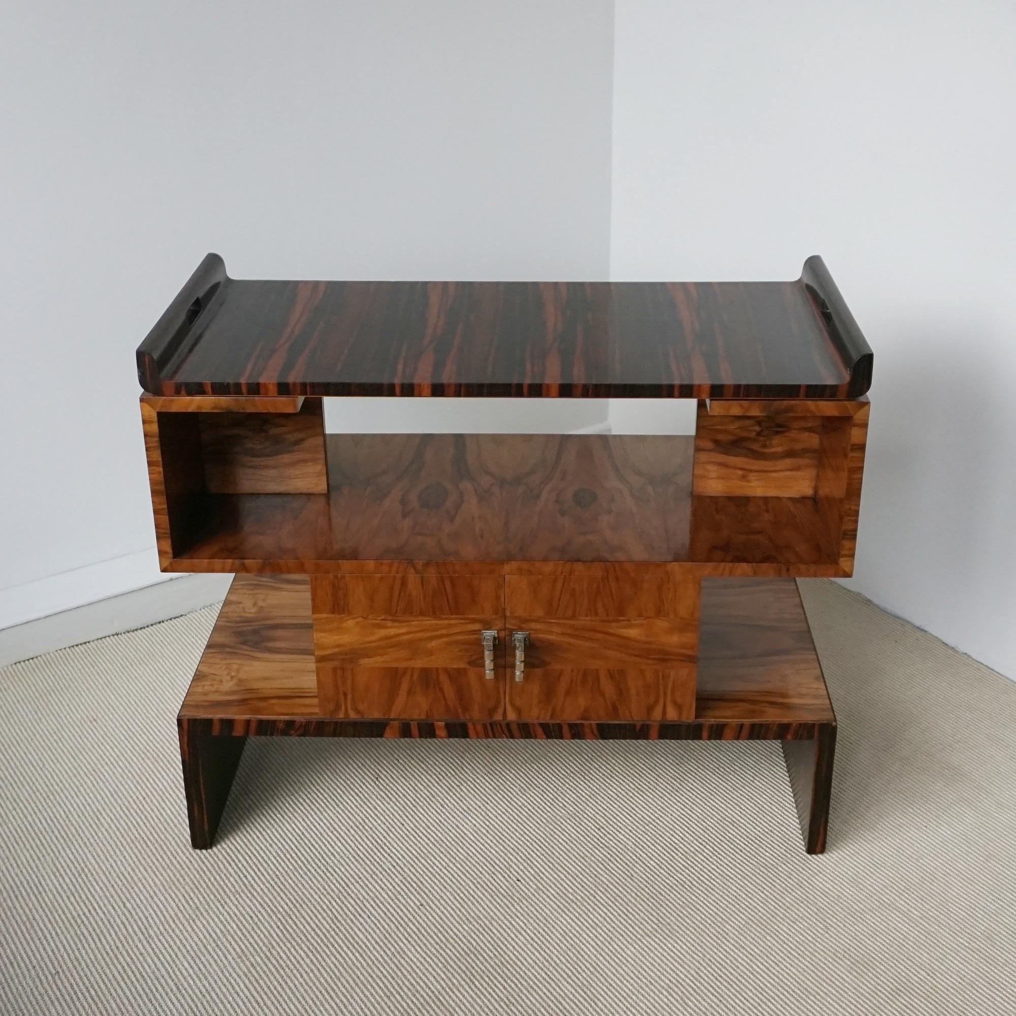 An Art Deco serving table comprising of a central double ended storage compartment with open shelving to either side and an upper detachable Macassar ebony serving tray. Burr walnut and Macassar veneered with original brass handles.

