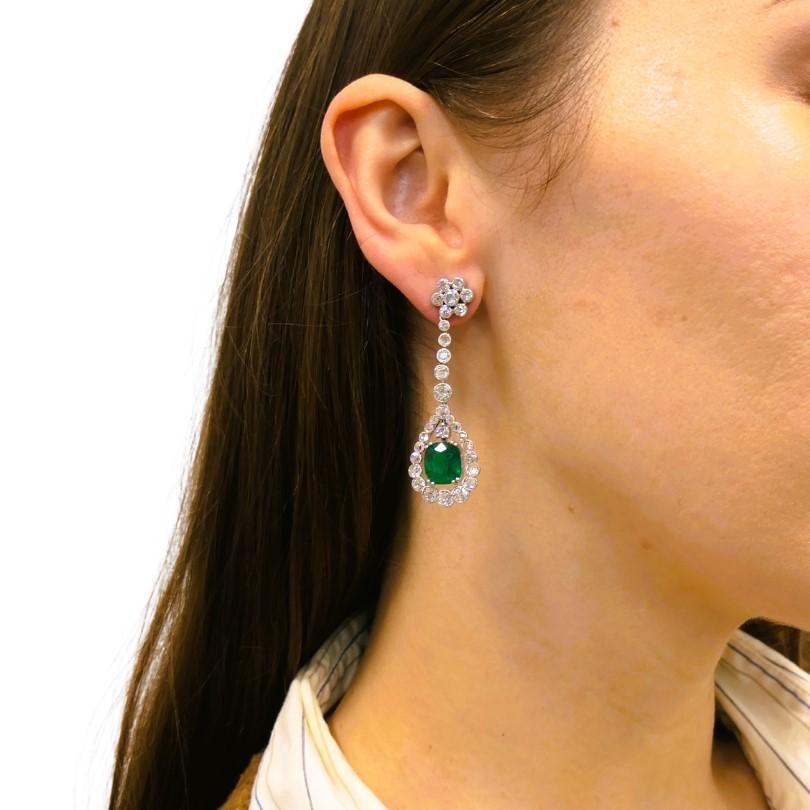 Impressive Art Deco drop earrings, made of platinum, featuring diamonds and cushion cut emeralds. 
Each emerald is surrounded by a halo of Old European and rose cut diamonds. The open settings give the gemstones space, emphasizing the geometry