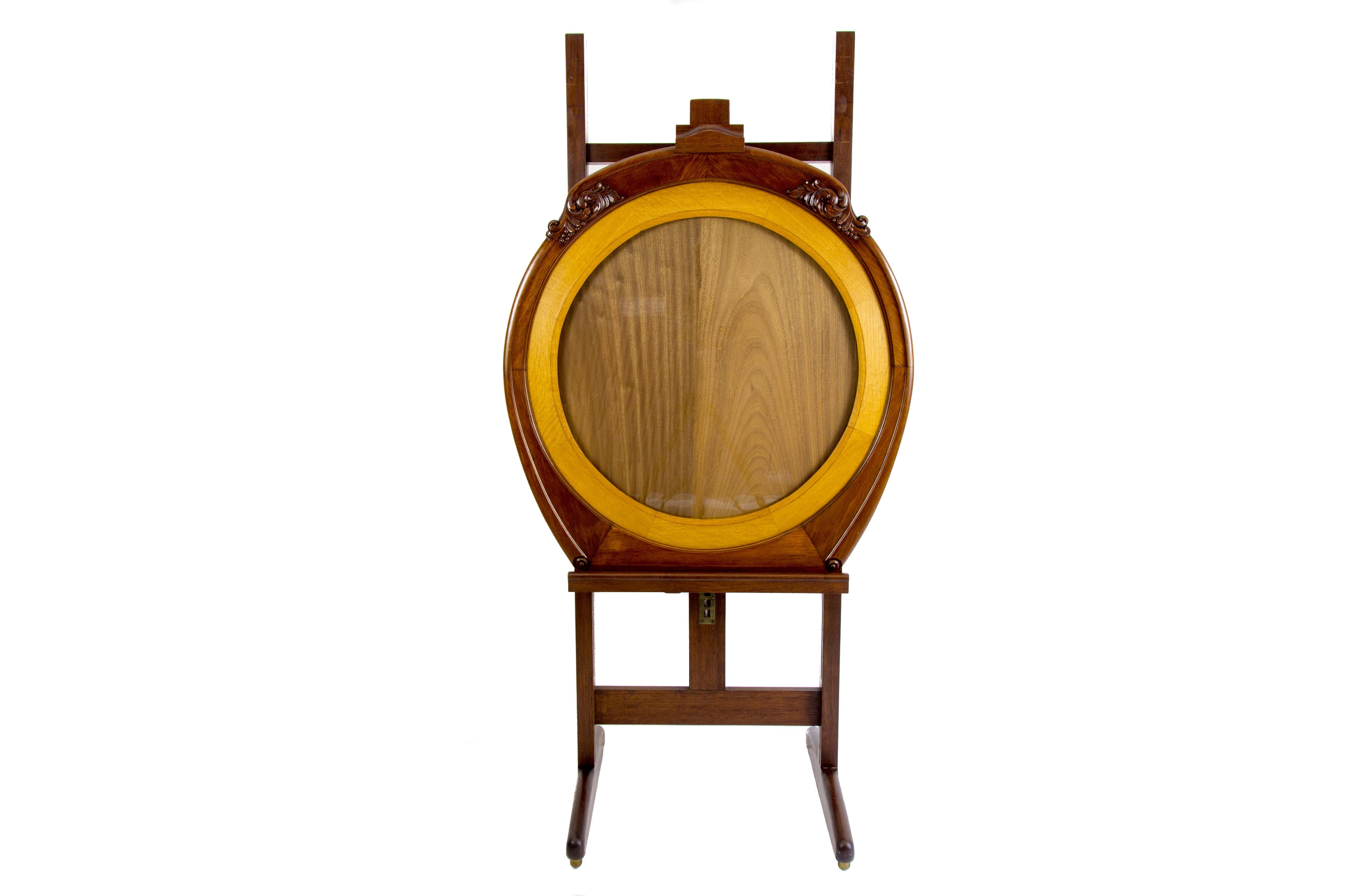 Rare Art Deco easel or painting stand from the 1920s, made of walnut and oakwood, comes together with the round frame with glass. The frame is decorated with floral carvings. Adjustable in height, this beautiful easel stands on four rollers. Can be