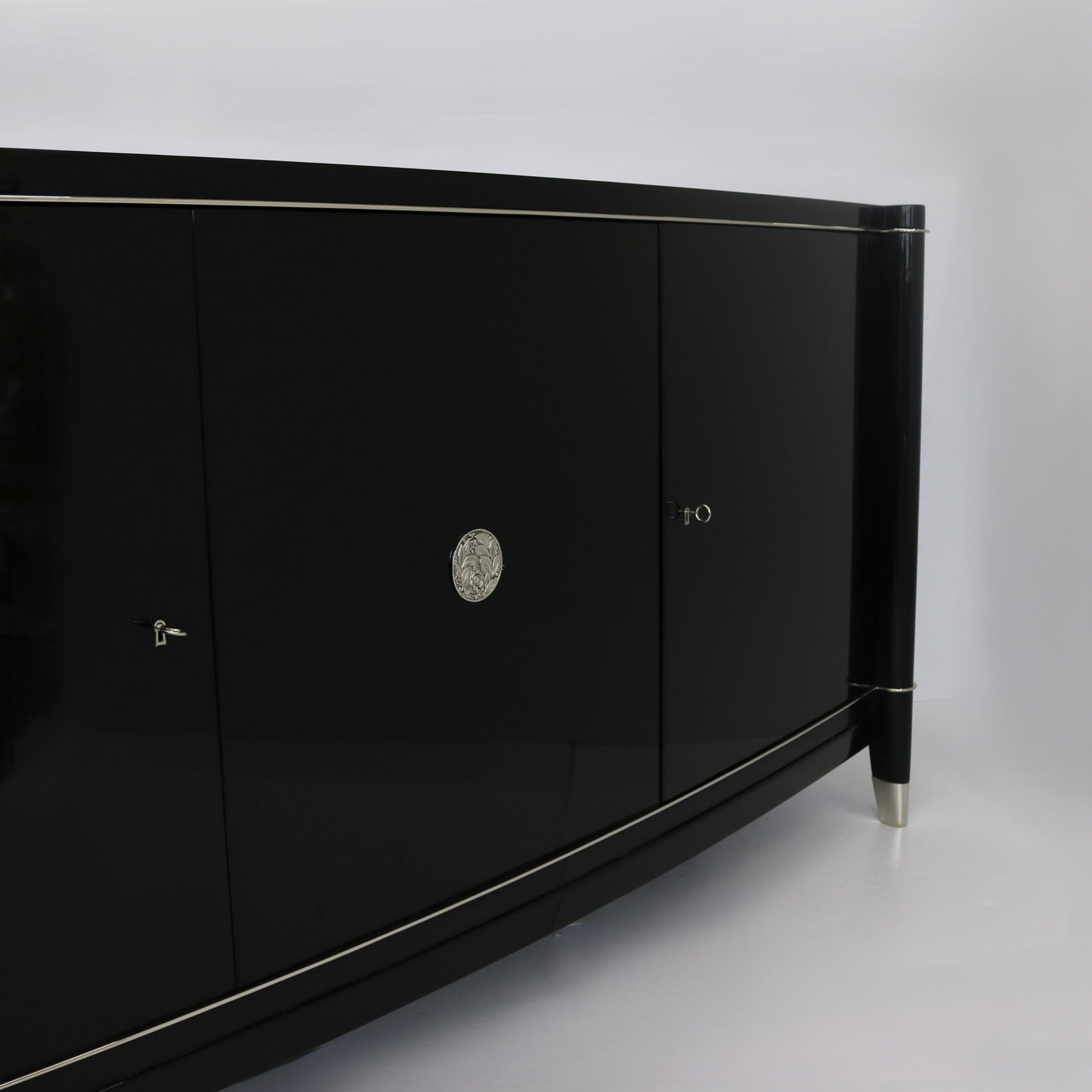 An elegant three-door De Coene Frères Sideboard with a delicate metal profile. The door is adorned with round fittings featuring a subtle floral motif. The sideboard has been polished to a high gloss finish and stands as a testament to the era's
