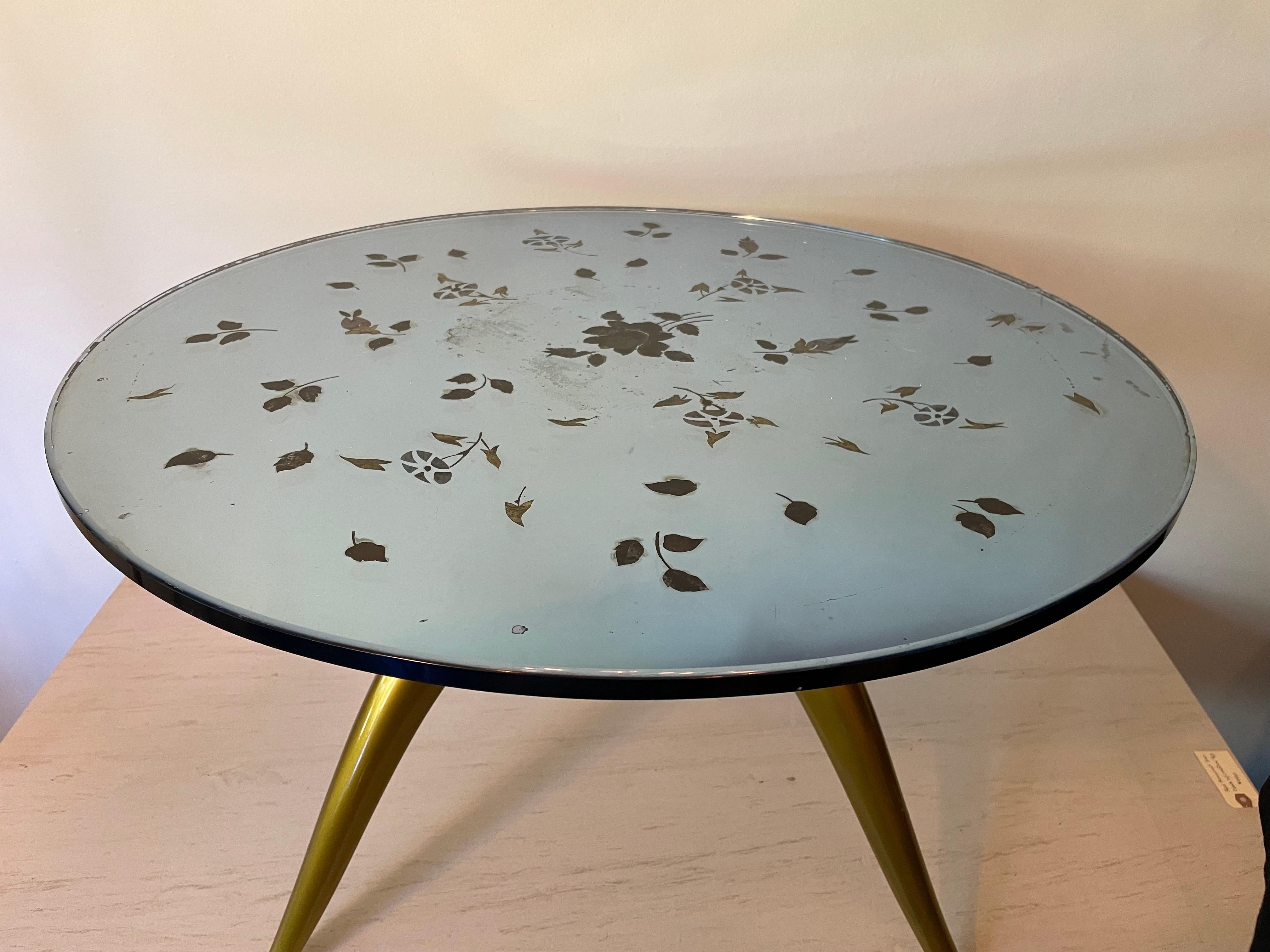 Dieser hübsche kleine Tisch ist ein wunderbarer Cocktail- oder Beistelltisch mit einer blassblauen, verspiegelten Glasplatte, die mit Blumen und einem Blattmotiv verziert ist. Der Sockel aus goldfarben lackiertem Holz wurde restauriert.
