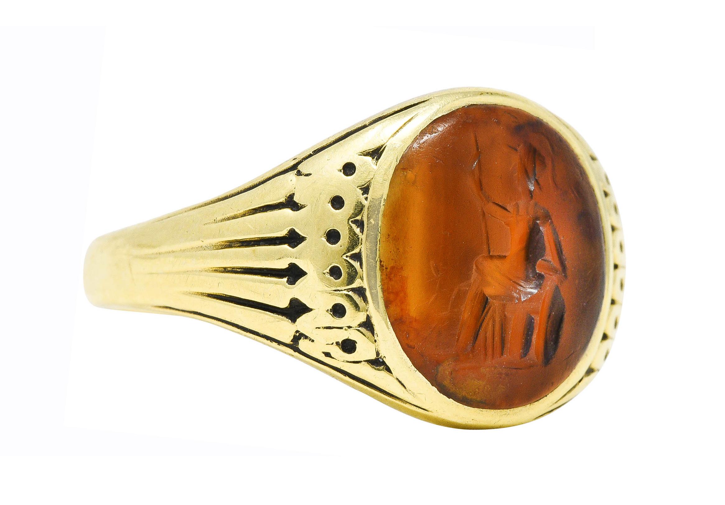Ring centers a 10.5 x 11.5 mm inlaid tablet of banded agate with a carved intaglio

Translucent brownish orange with medium saturation and subtle banding

Depicting a seated pharaoh figure with staff and draped robes

Flanked by decoratively