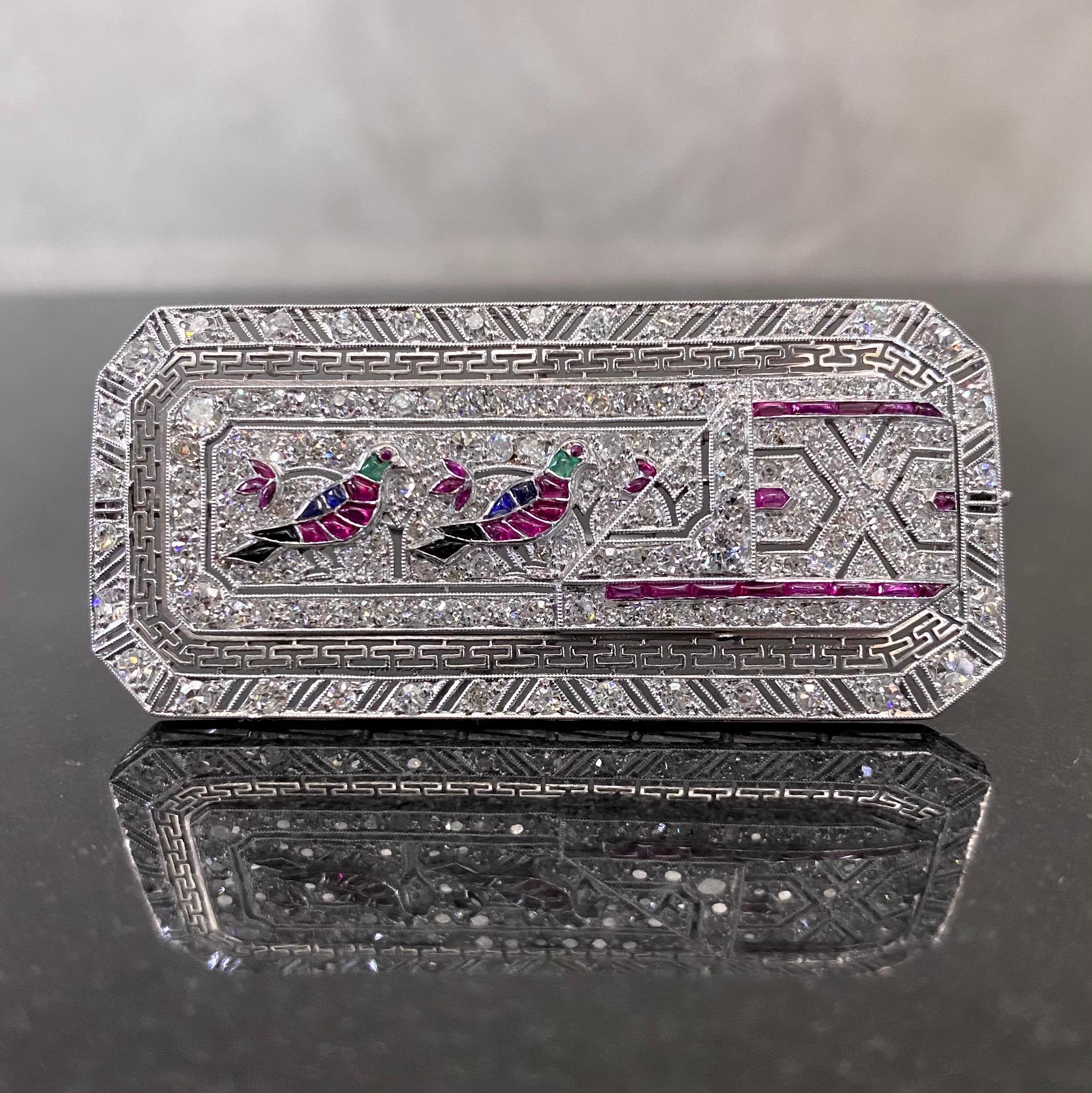 Egyptian Revival diamond and gem-set brooch in platinum. This geometric plaque brooch of an octagonal design is modelled as two hieroglyphic swallow birds decorated with calibre-cut rubies, sapphires, emeralds and onyx, further accented with ruby