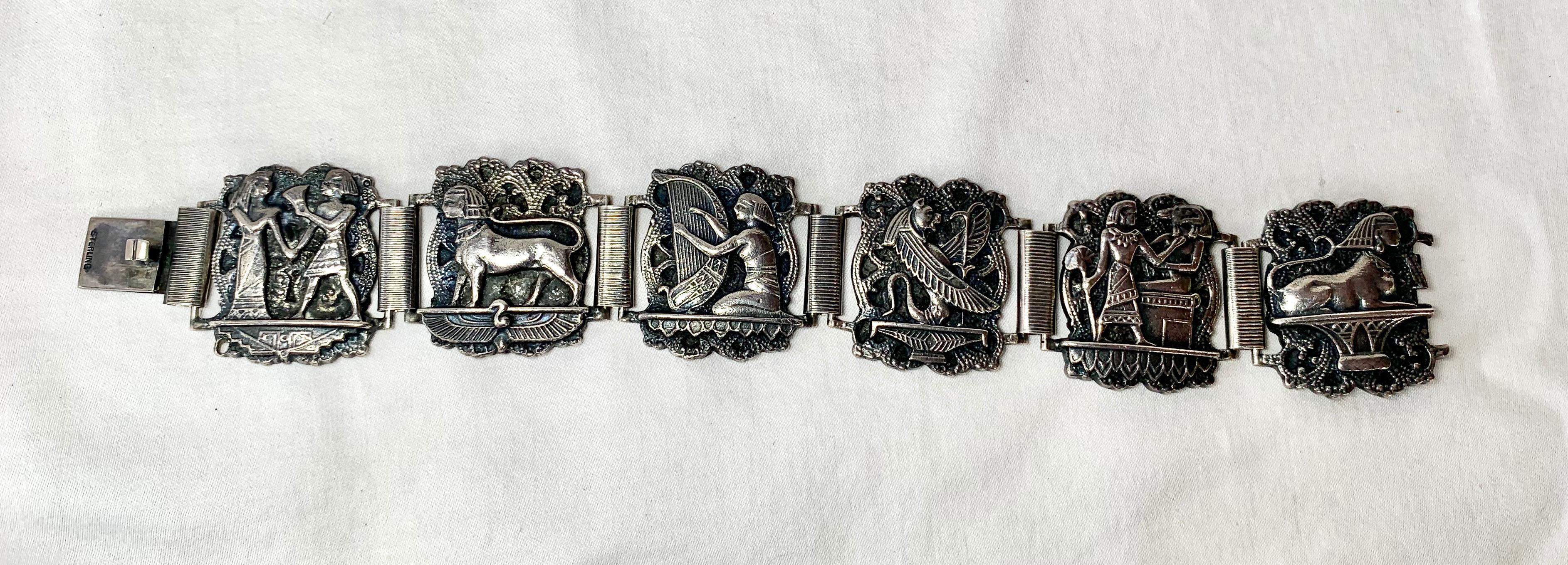 Un meraviglioso bracciale antico Art Deco Egyptian Revival con spettacolari immagini dell'Antico Egitto in argento sterling.  Le immagini includono una sfinge che cammina e giace, il dio gatto Bastet o Bast, un suonatore di lira o arpa e una