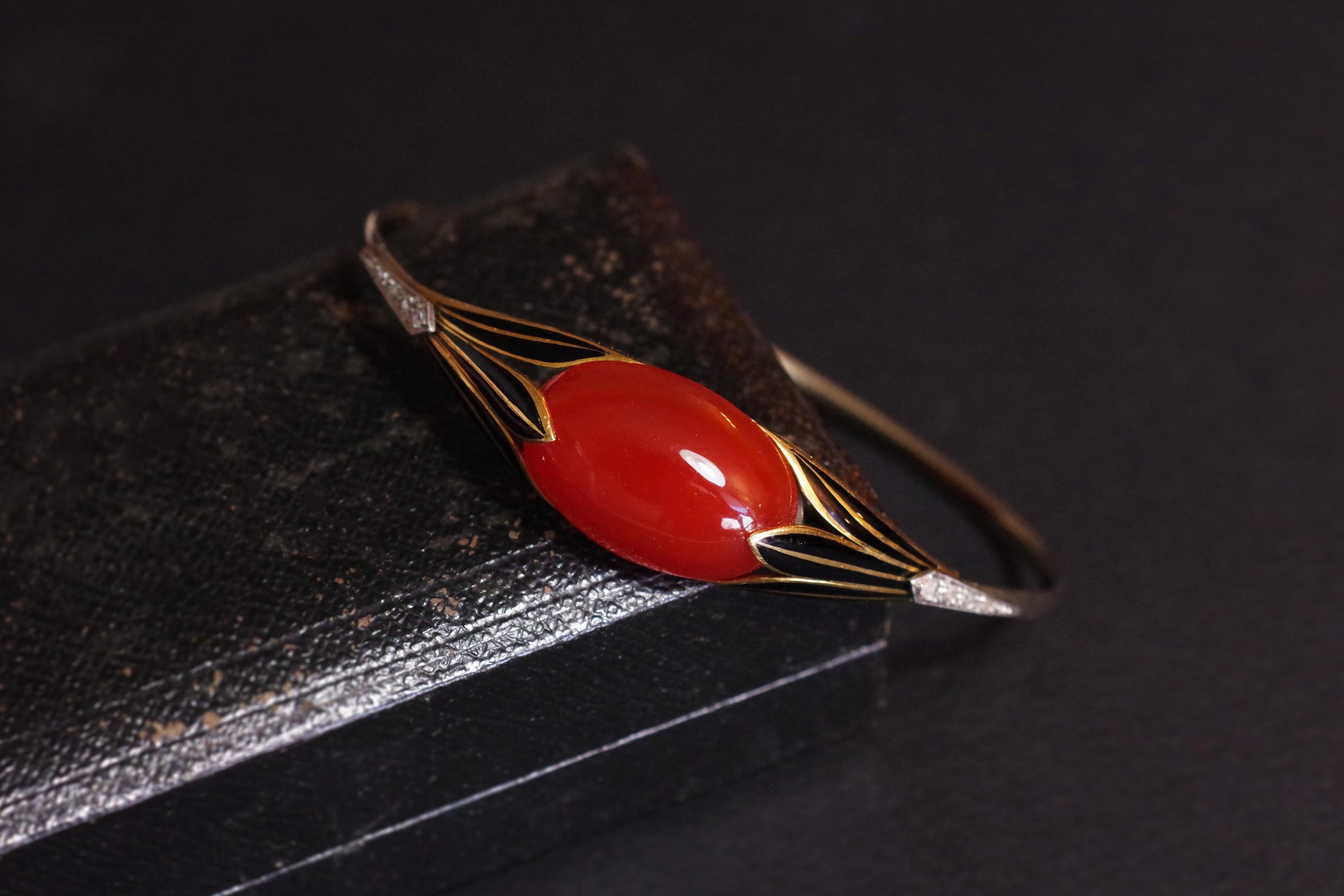 Art Deco Egyptomania bracelet in 18 karats white gold. This rare bangle bracelet is adorned with a large carnelian cabochon in the center, held on each side by a yellow gold palmette and enameled in black. The palmettes are set with eight rose-cut