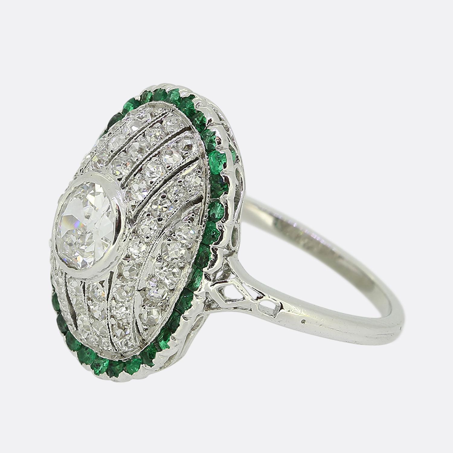 Here we have a fabulous emerald and diamond cluster ring crafted during pinnacle of the Art Deco movement. A single round faceted old European cut diamond sits slightly risen at the centre of the face in a full bezel setting. This principal stone