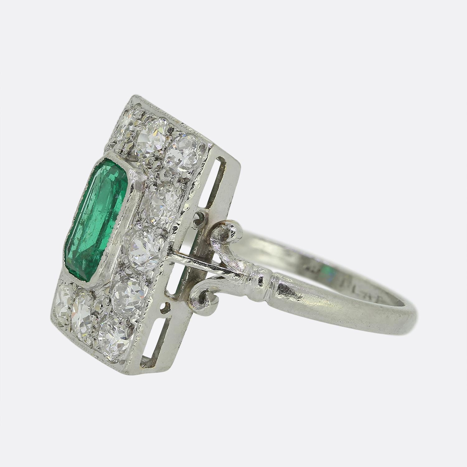 Here we have a delightful emerald and diamond cluster ring crafted during the pinnacle of the Art deco movement. This platinum piece showcases a single emerald cut natural emerald at the centre of the face and showcases a rich vivid green colour.