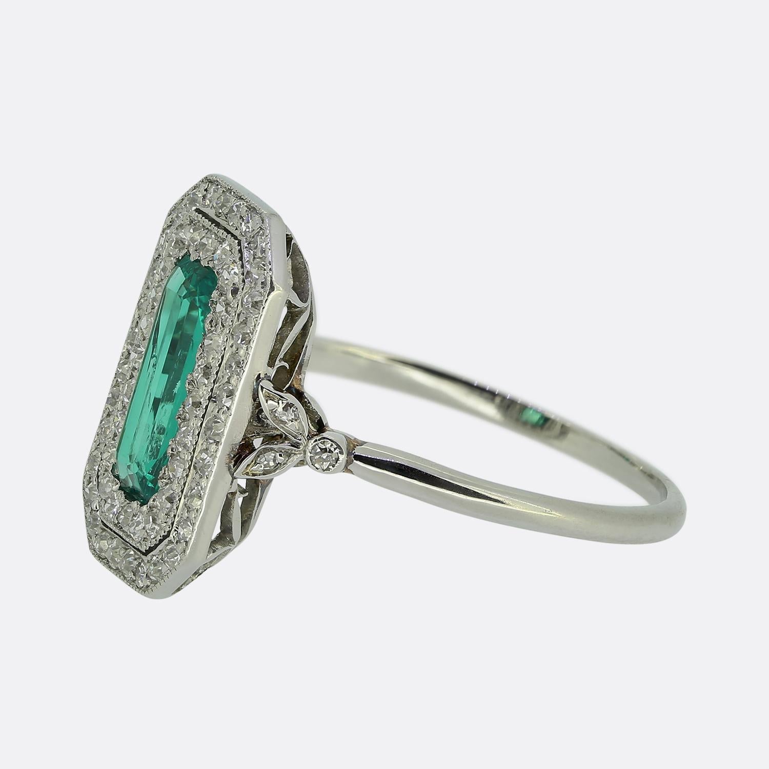Here we have an exquisite elongated cluster ring crafted during the Art Deco movement. This 18ct white gold piece prominently features a vibrant green emerald, elegantly set at the centre of the face. Surrounding this principal stone is a double