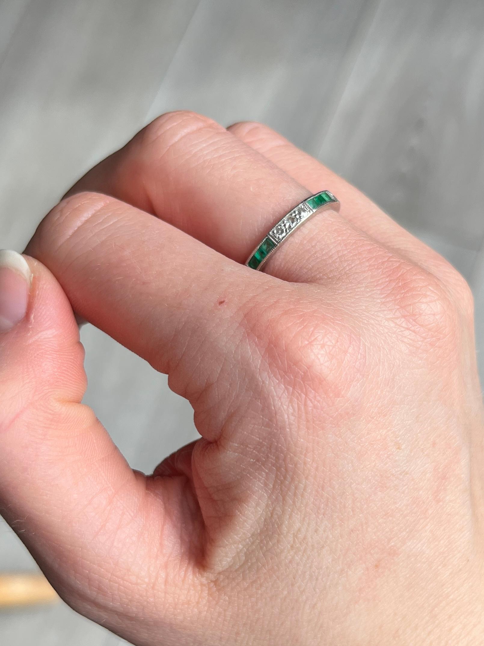 A stunning Art Deco eternity band ring set with emeralds and diamonds. Alternating collections of three square cut green emeralds measuring 5pts each are set between a trios of round-cut white diamonds measuring 3pts each. The stones are set around