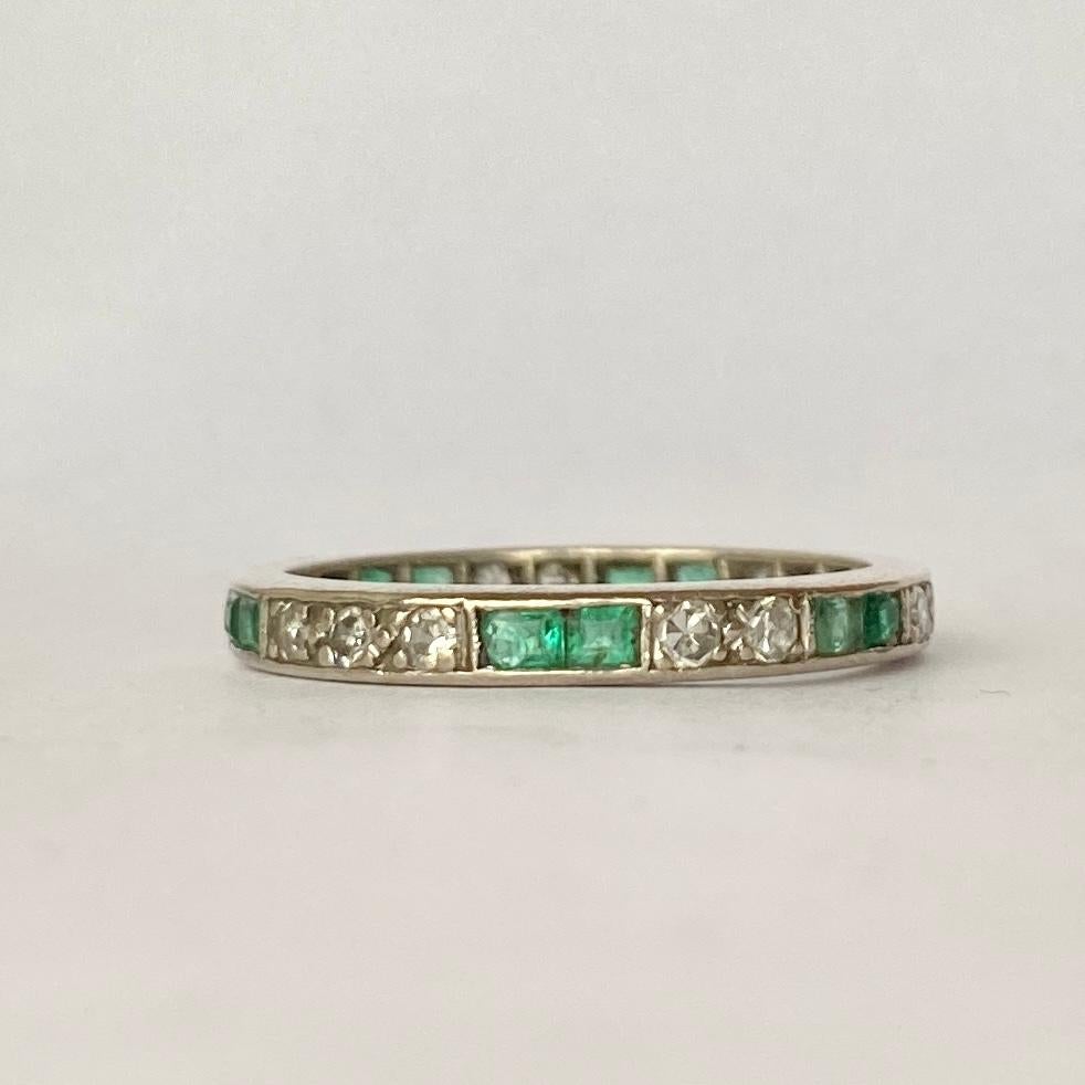 A stunning Art Deco eternity band ring fully set with emeralds and diamonds. Alternating duos of square cut green emeralds measuring 10pts each are set between a trios and duos of round-cut white diamonds measuring 5pts each all around this