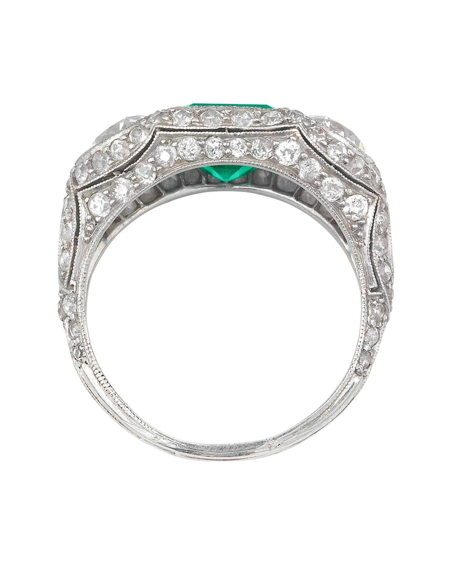 This striking emerald and diamond ring captures the timeless sophistication of the Art Deco style. Mounted in an ornate platinum dome setting, a magnificent emerald, weighing approximately 2.00 carats, is joined by two spectacular European cut