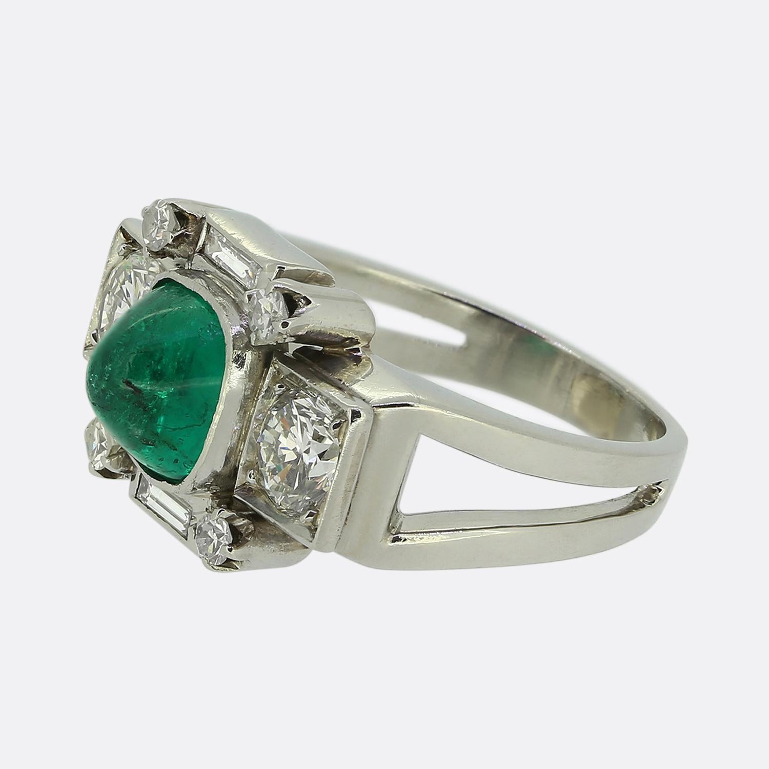 Here we have a wonderfully unique emerald and diamond ring crafted during later stages of the Art Deco movement. A single sugarloaf cabochon emerald possessing a glorious green colour tone sits slightly risen at the centre of the face and is flanked