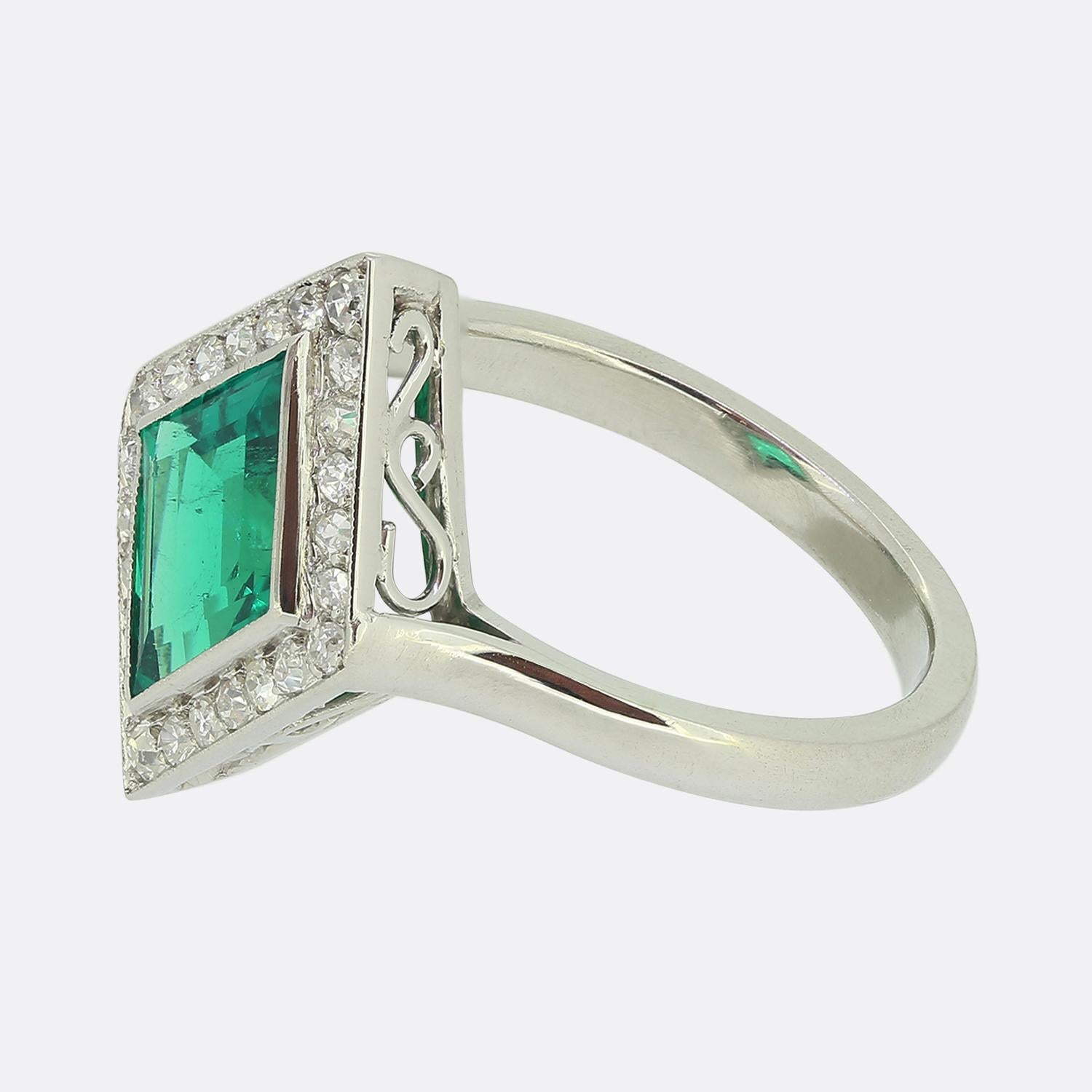 Here we have a marvellous cluster ring taken from a time when the Art Deco style was revolutionising the world of design. A single lozenge shaped emerald of Colombian origin sits slightly risen at the centre of the face showcasing a rich vivid green