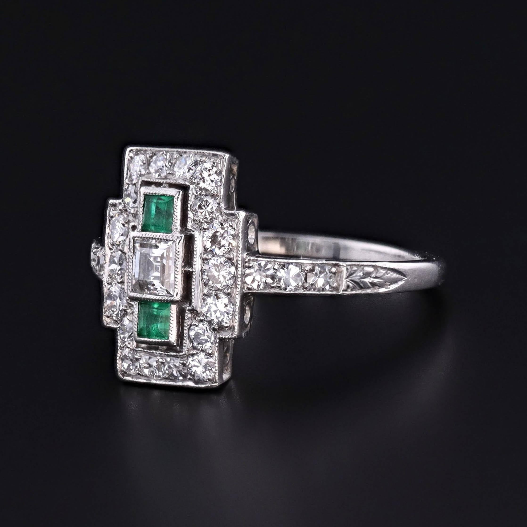 Dieser geometrische und raffinierte Art-Déco-Ring (um 1920) zeigt zwei lebhafte quadratische Smaragde im Stufenschliff und einen quadratischen Diamanten im Stufenschliff von 0,22 ct. der Farbe F und der Reinheit VVS, umgeben von 18