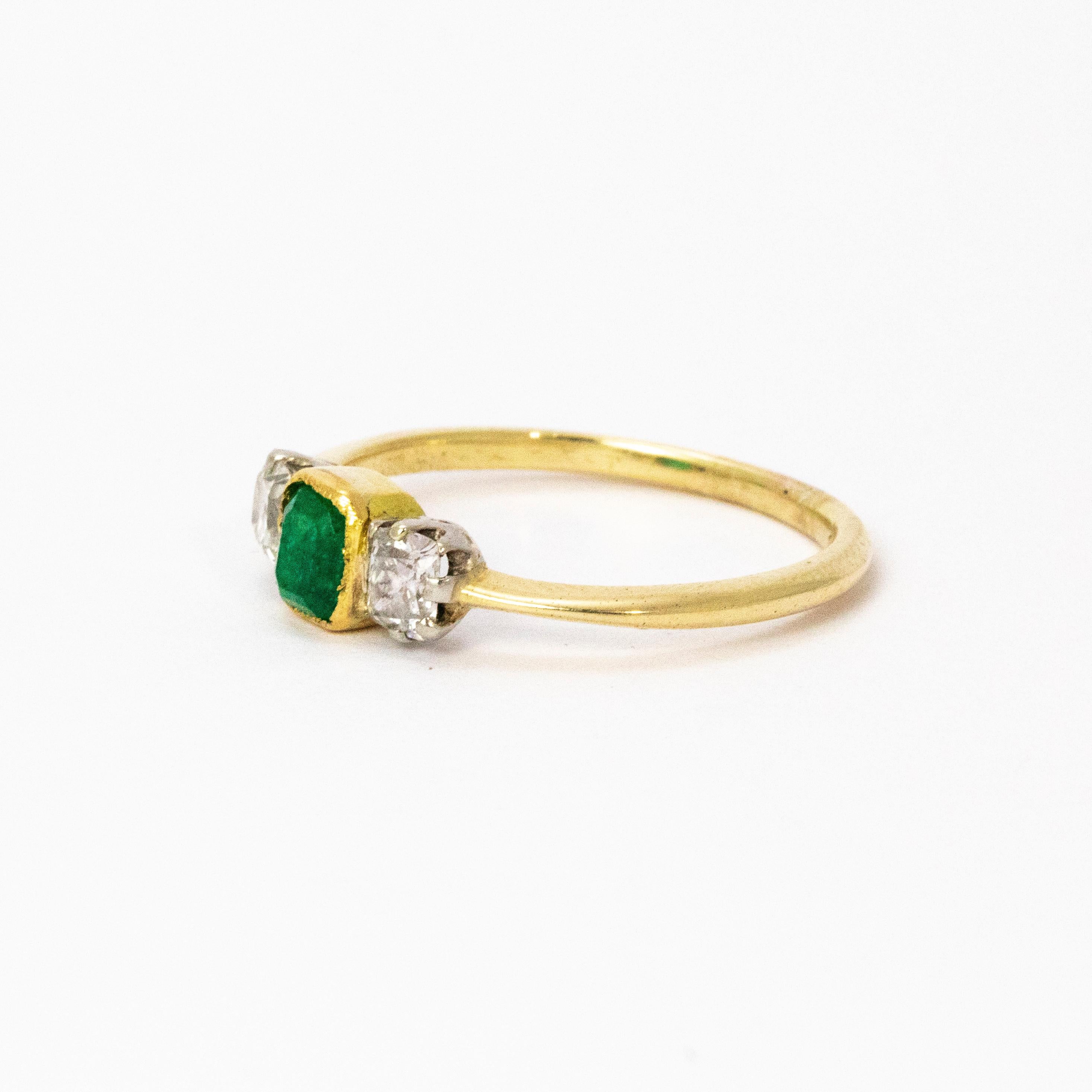 An elegant emerald and diamond three-stone ring crafted circa 1920. The fine central emerald measures approximately 45 points and has a good green colour. Flanking the central stone are two beautiful square old mine cute diamonds measuring a total