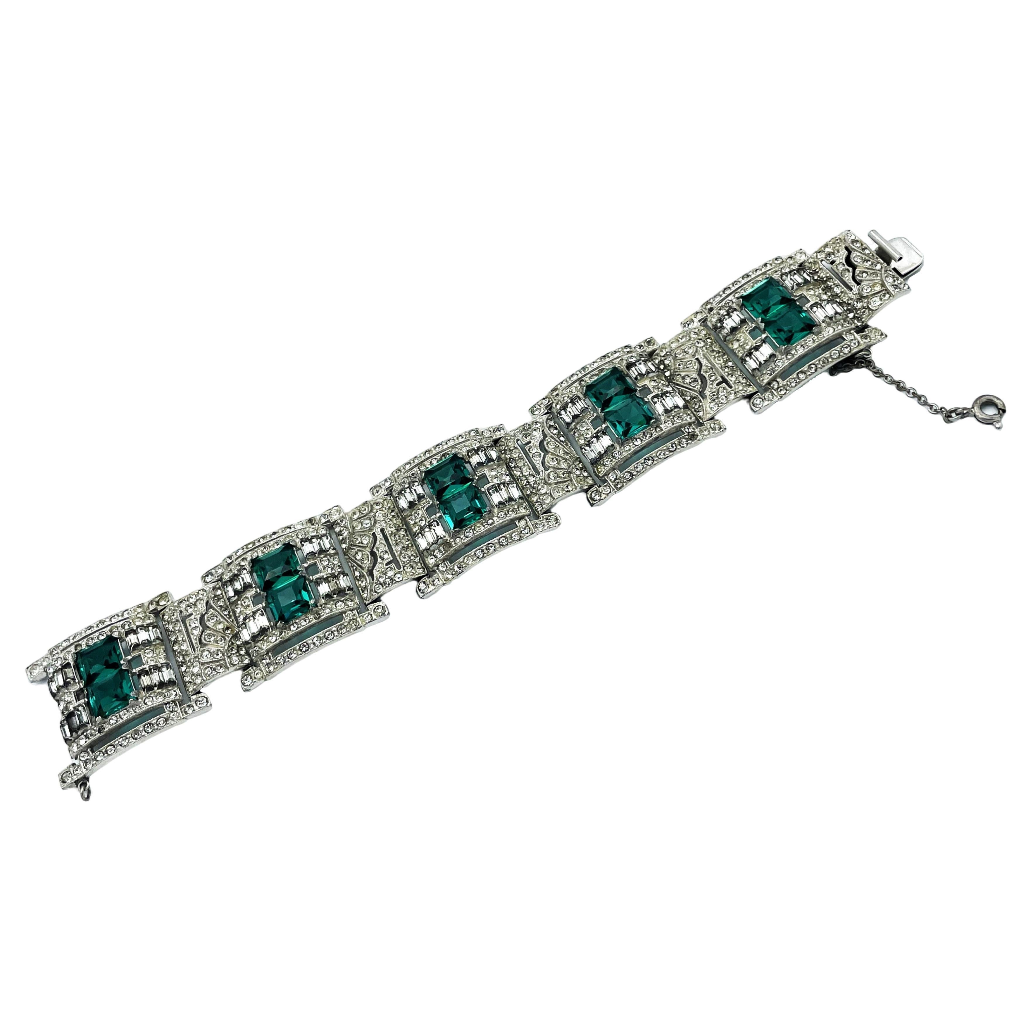 Un superbe bracelet de voyage Art Déco des années 1920 réalisé dans le style de la haute joaillerie : un bracelet en métal rhodié et en pâte française imitant les diamants et les émeraudes. Fermoir à ressort avec chaîne de sécurité