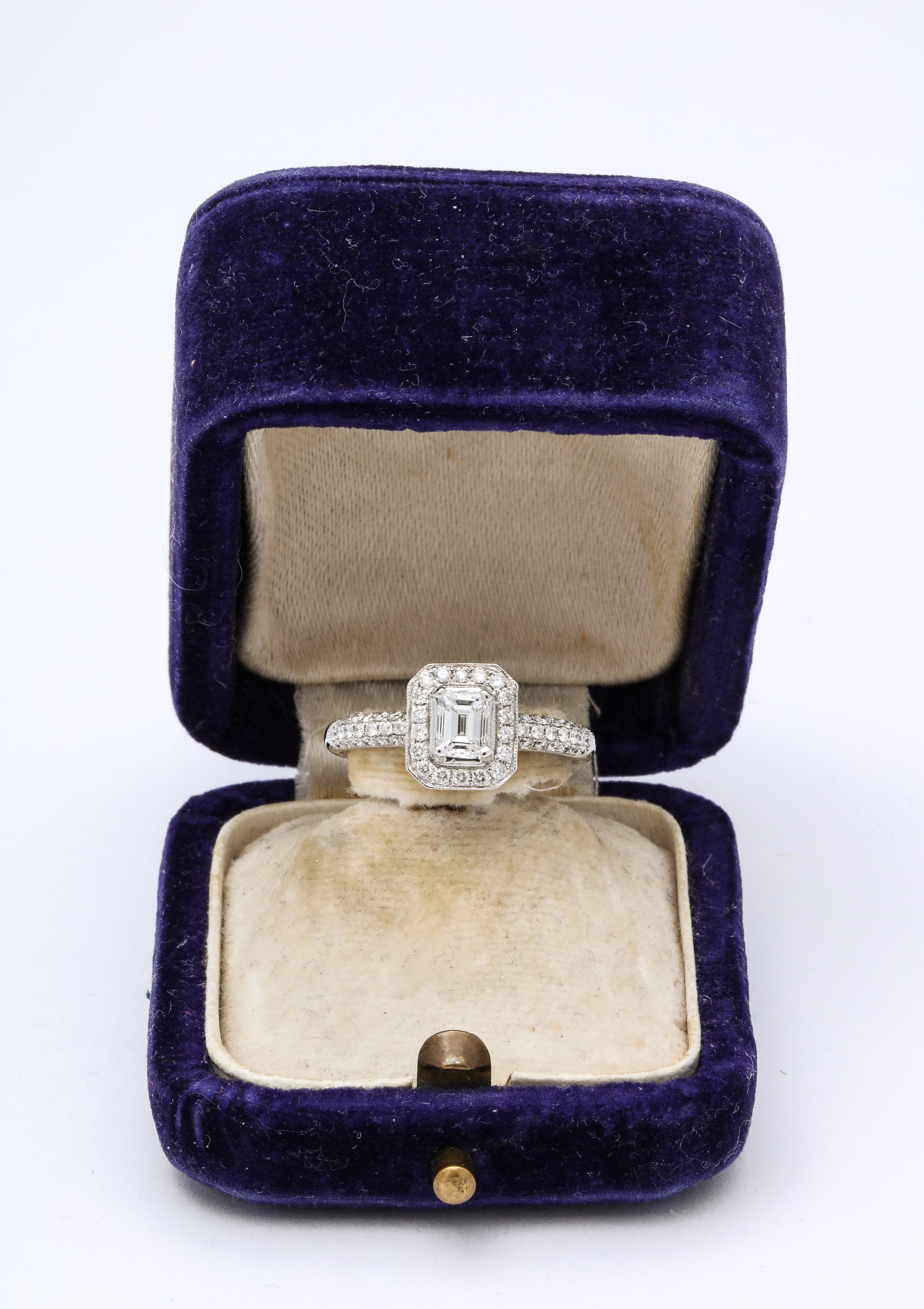 Verlobungsring mit Smaragdschliff und 18k Weißgold. Ein glänzender VS I Diamant-Verlobungsring. Ein zentraler Diamant im Smaragdschliff (0,50) wird von einer Gruppe kleinerer Diamanten umrahmt, die in eine Weißgoldfassung eingesetzt sind.