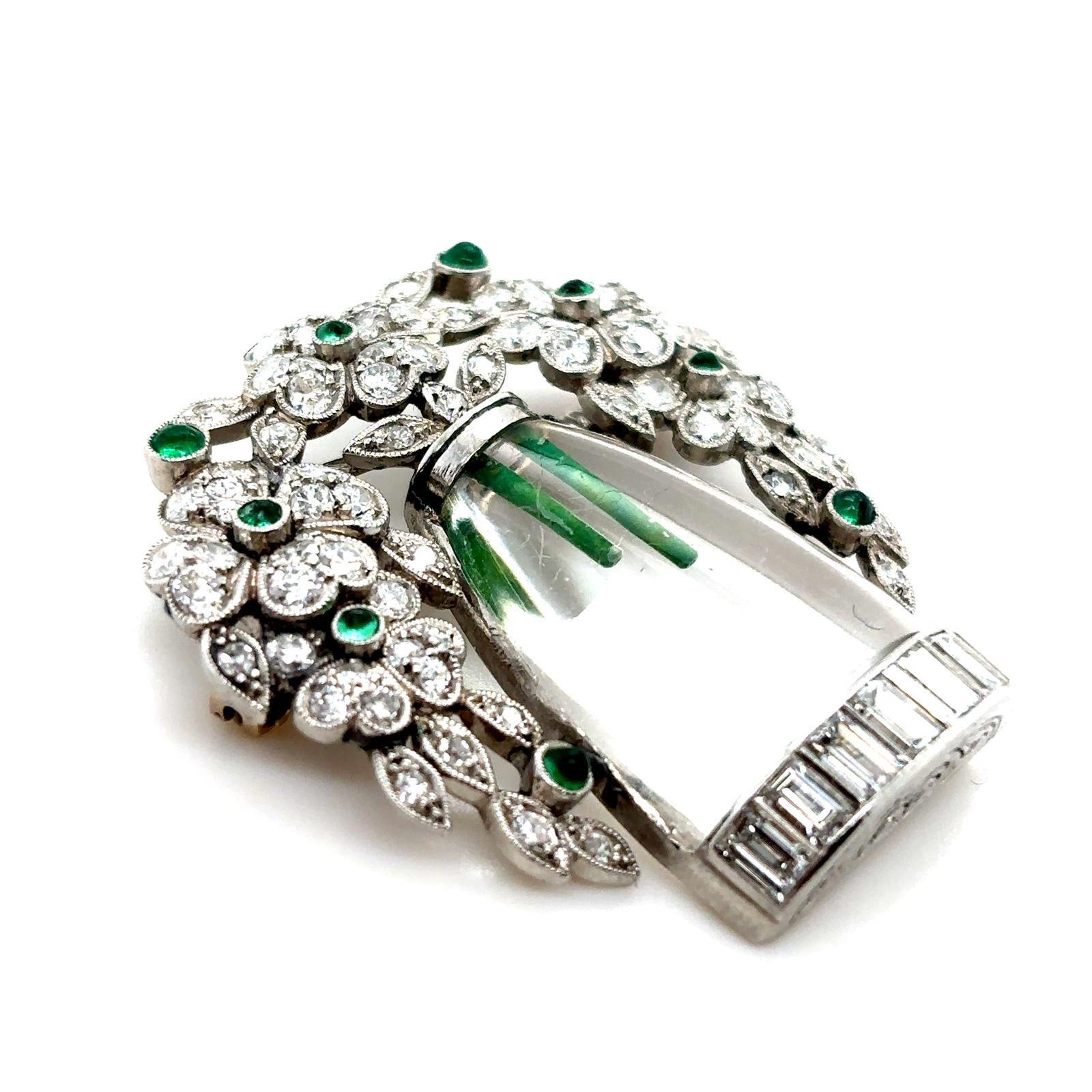 An Art Deco emerald, diamond and crystal flower vase platinum brooch 

This exceptional and unusual brooch is designed as a bouquet of flowers in a vase, the blooms cascading down the sides of the gently curved hand painted crystal vase, grain and