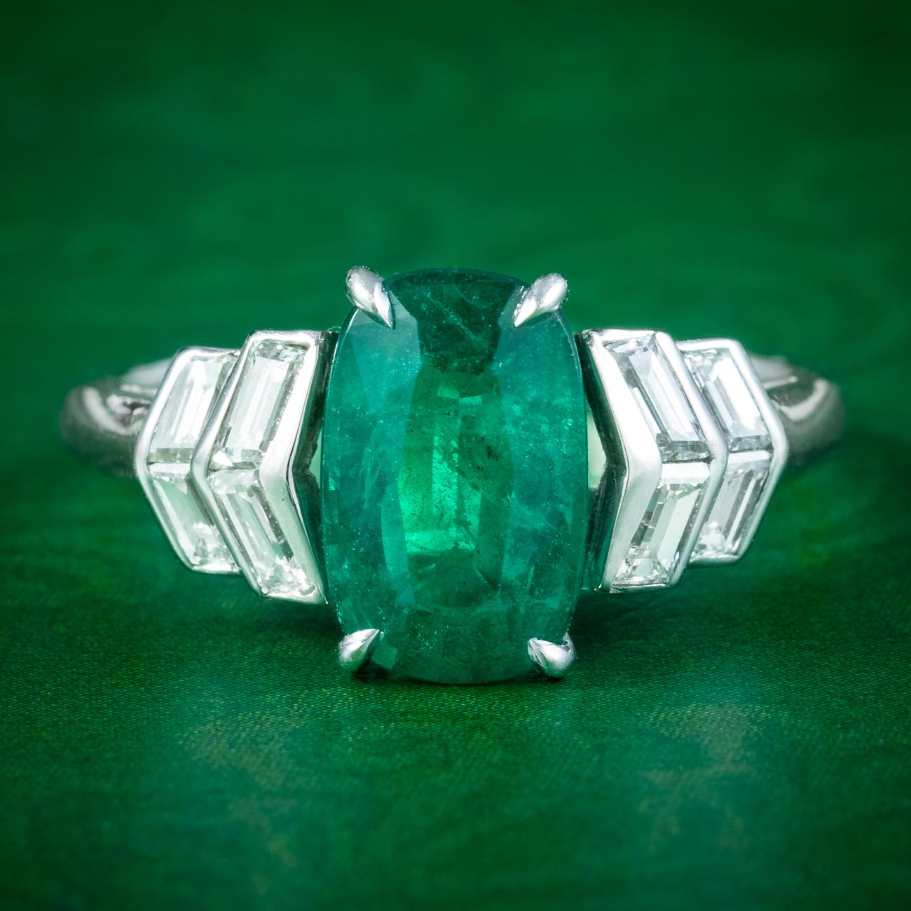 A striking Art Deco ring adorned with a natural cushion cut emerald in the centre flanked by chevron shoulders bezel set with eight step cut diamonds. All the stones test as natural and are detailed in the accompanying gem certification.

The