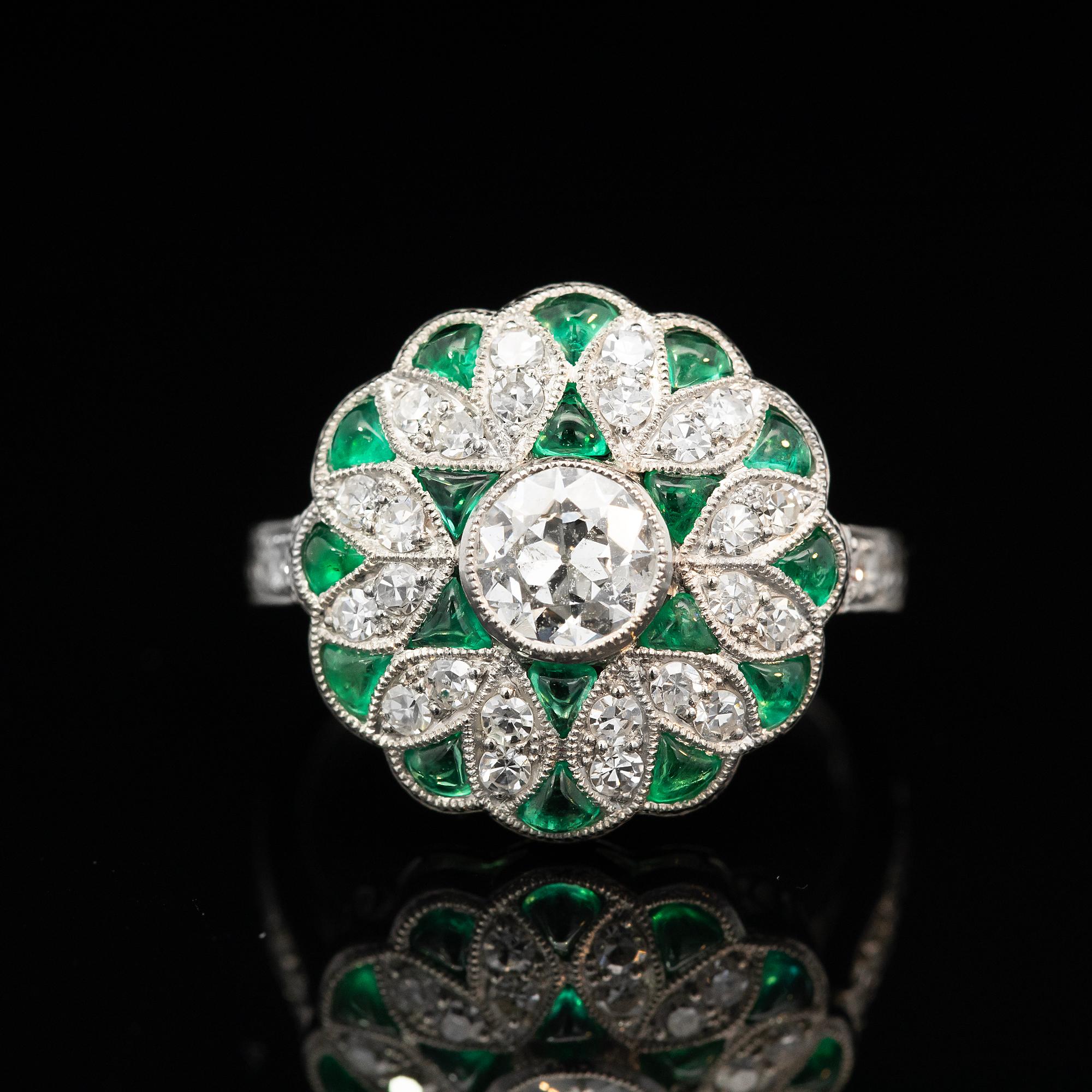 True its era, this Art Deco cluster ring makes an elegant statement piece. Featuring grain set early European cut and single cut diamonds with beautiful green emeralds.

Diamond: One early European cut, I-J colour, I1 material, estimated weight