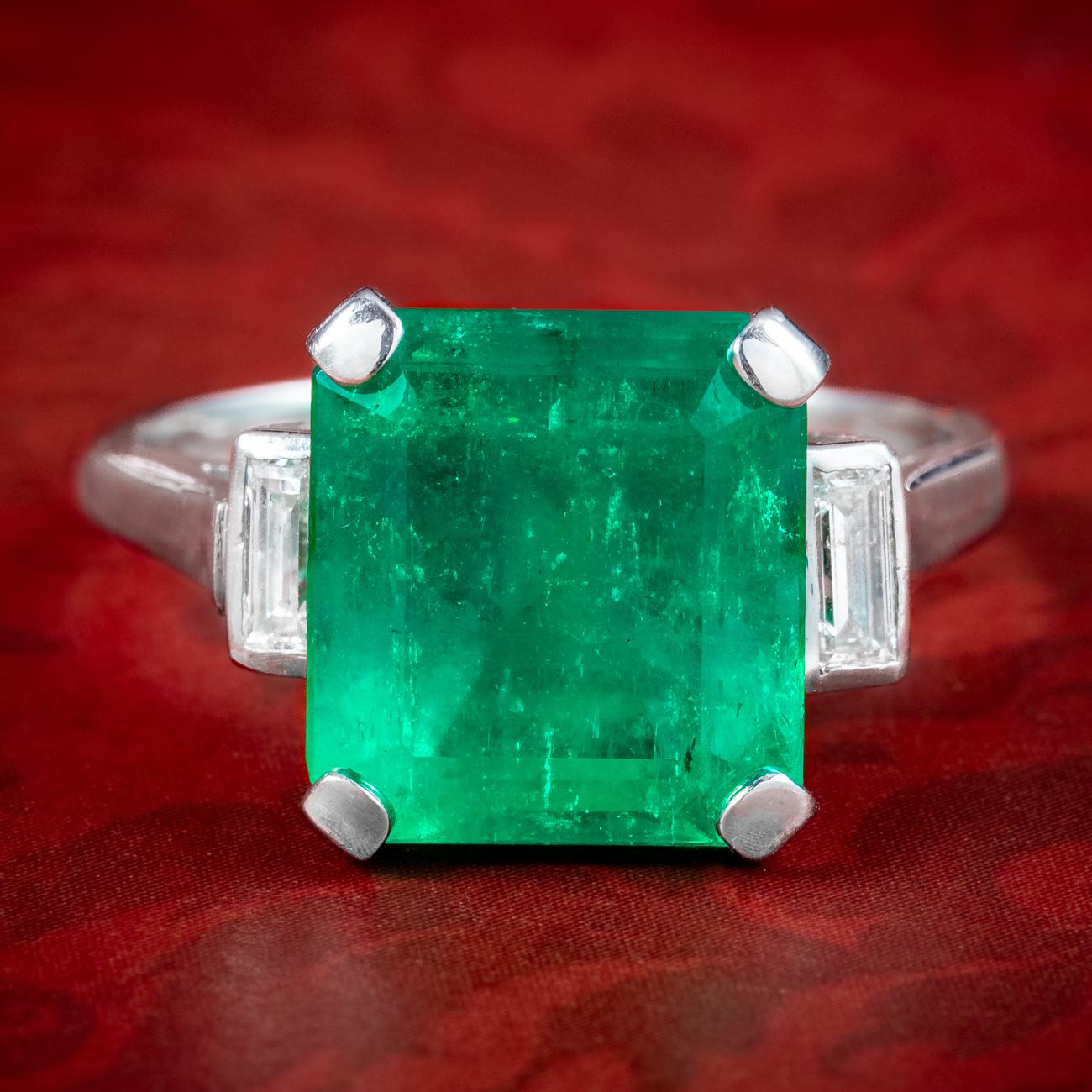 A magnificent Art Deco trilogy ring boasting a striking Colombian step cut emerald with an intense green hue. The stone is accompanied by a comprehensive gem certification that verifies it’s a natural Colombian emerald, weighing an impressive 7.24