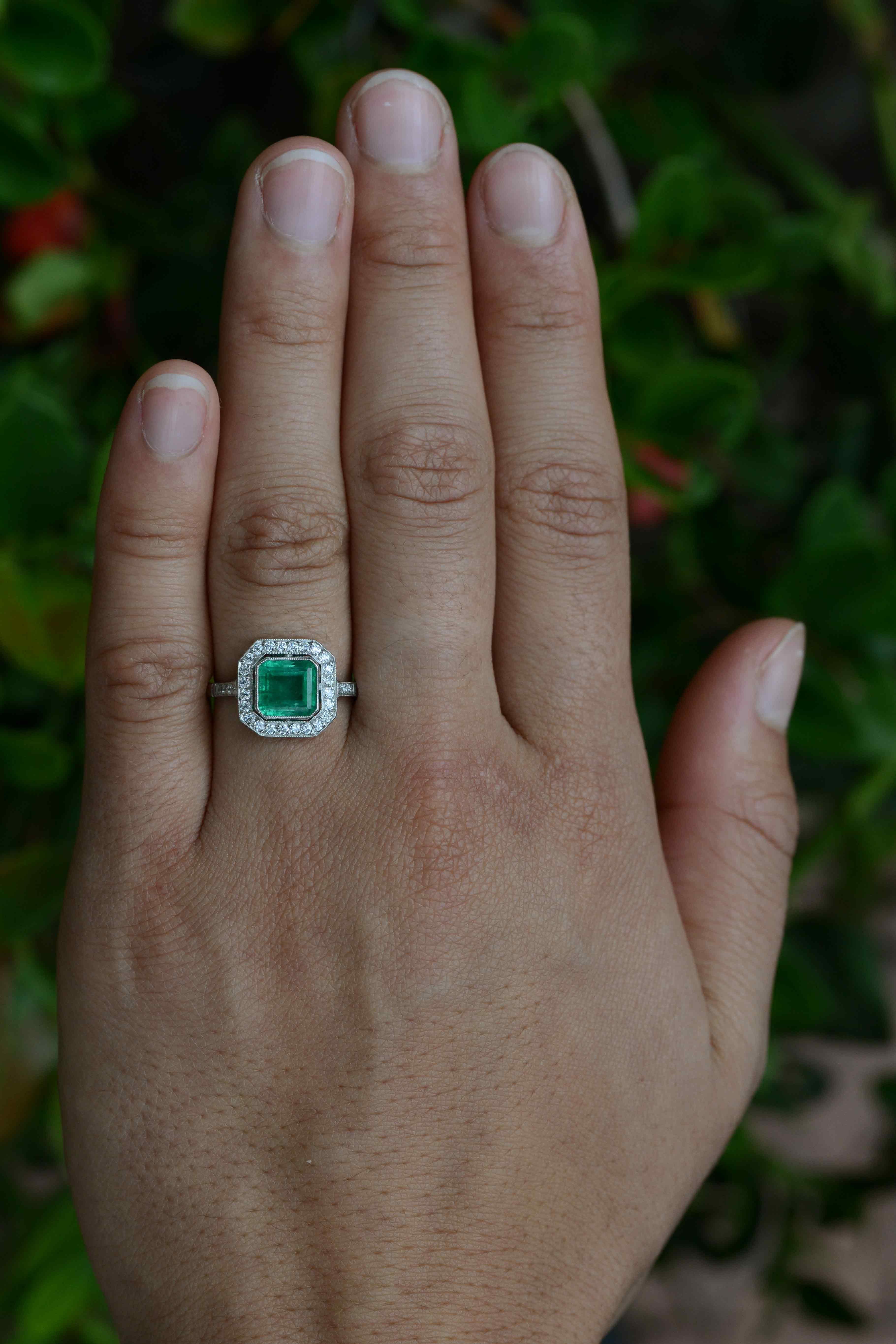 A breathtaking grass-green Colombian emerald takes center stage in this striking Art Deco style emerald engagement ring. The platinum setting features a sizable 1.56 carat gemstone that glows with light from within its soul. Floating in a milgrain