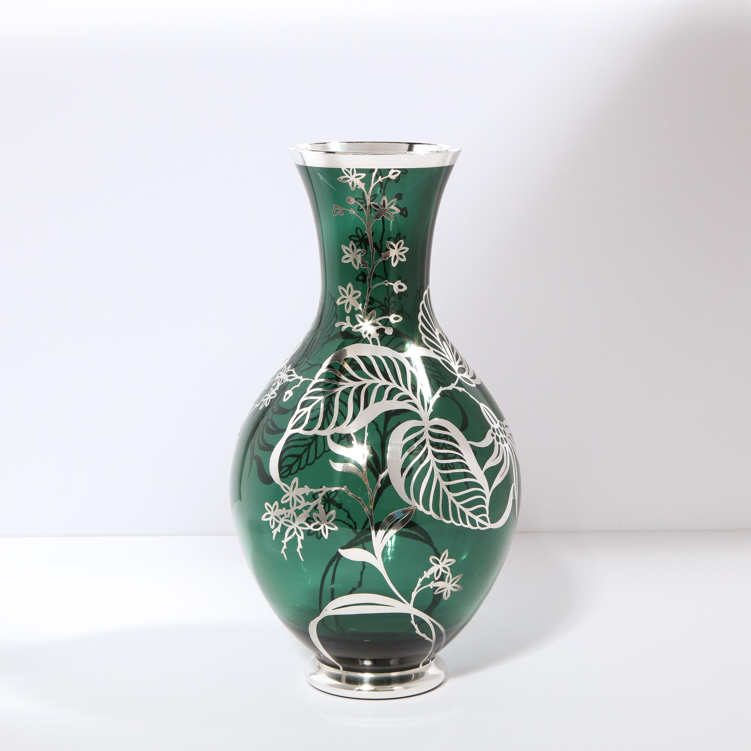 This stunning Art Deco emerald glass vase was realized in the United States circa 1940. It features an undulating body with a circular mouth banded in sterling silver with a matching base. The vase has been realized in translucent emerald glass with