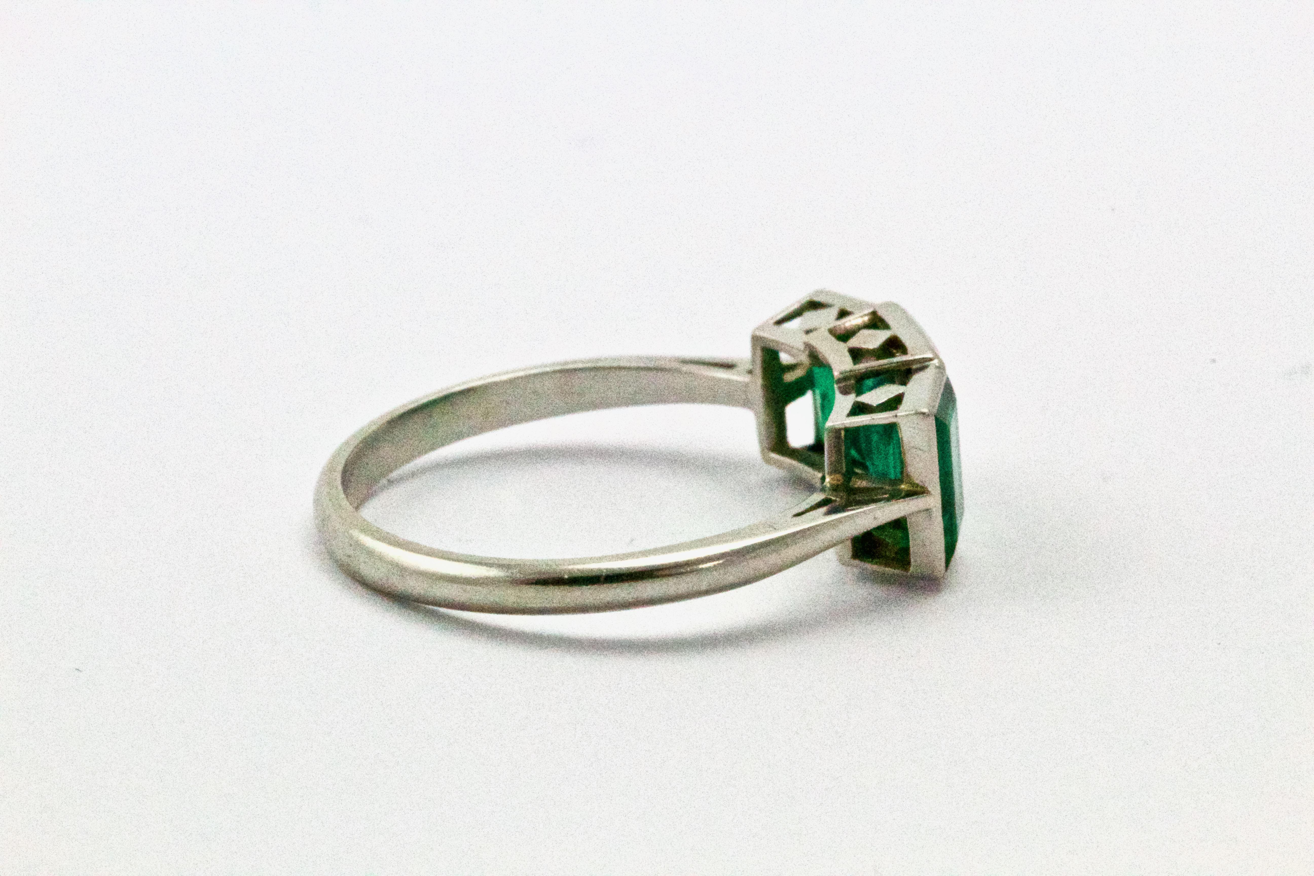 A mesmerising Art Deco era Emerald trinity ring. Each stone, step cut and channel set - displays an excellent deep green colour. Approx 1.5 carats total. An incredibly stylish 1920s take on the classic three-stone, modelled in platinum