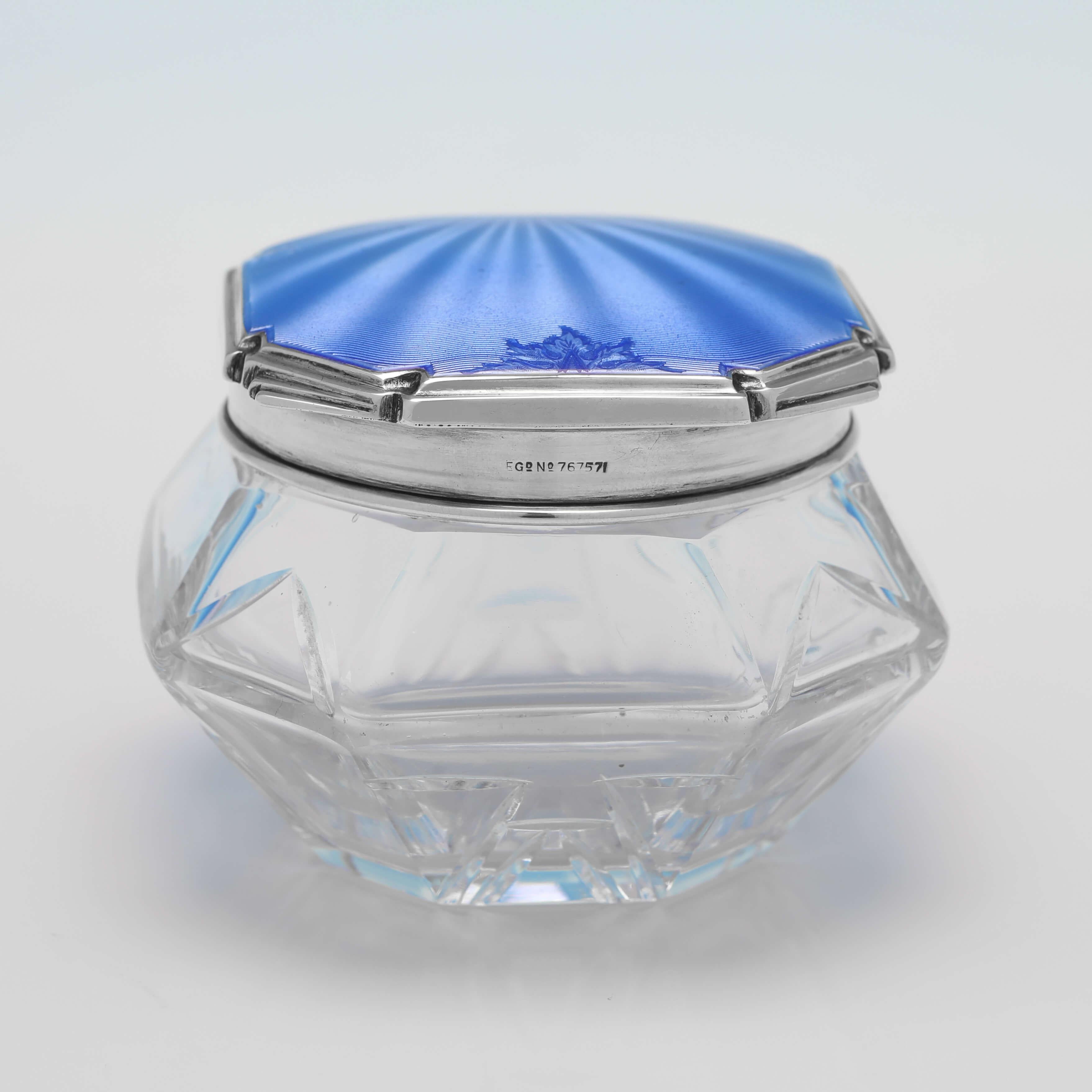 Hallmarked in Sheffield in 1933 by Walker & Hall, this stunning, Glass & Sterling Silver Dressing Table Jar, features a very stylish Art Deco enamel lid, and an angular glass body. 

The dressing table jar measures 2.75