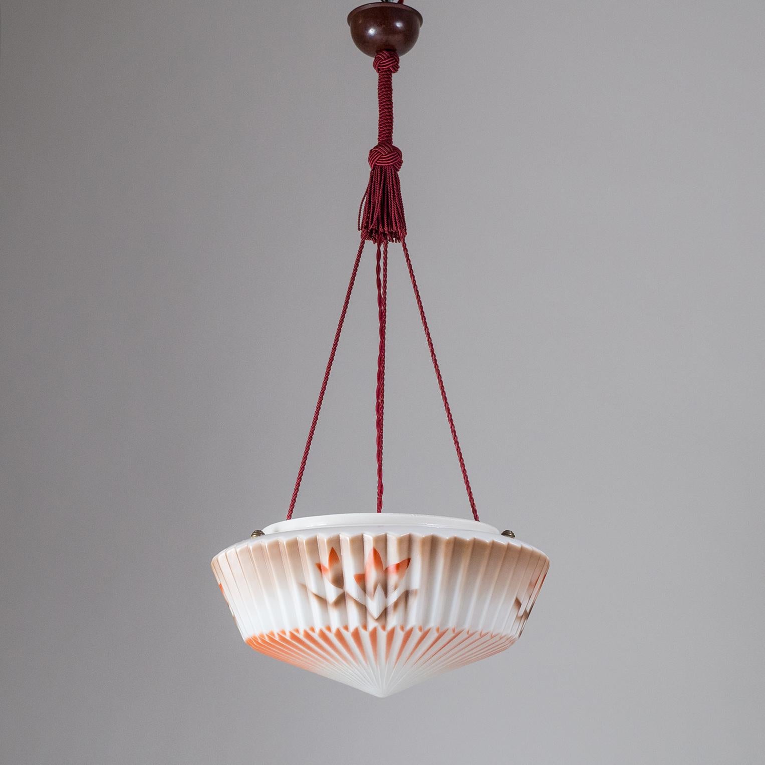 Very unique Art Deco suspension lamp, circa 1930. A large 'pleated' glass bowl is suspended by bordeaux colored cords with matching tassels and a bakelite canopy. The diffuser has an intricate dual color 'aerography' decor, accentuating the pleated