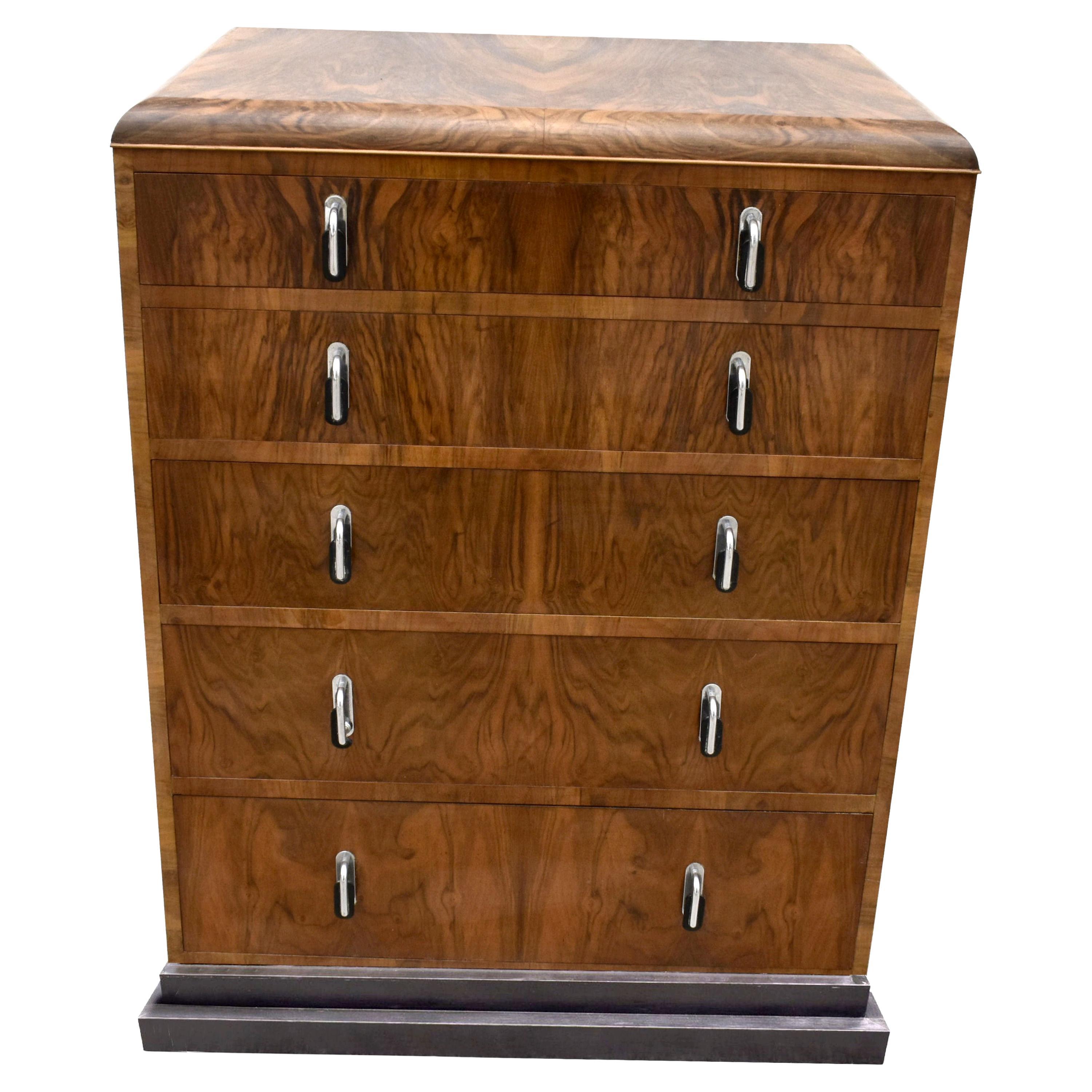 Very stylish Art Deco walnut chest of drawers originating from England and dating to the 1930's. It has stunning walnut veneers and great original Art Deco handles in chrome and black bakelite. Great stepped design to the stepped ebonized plinth