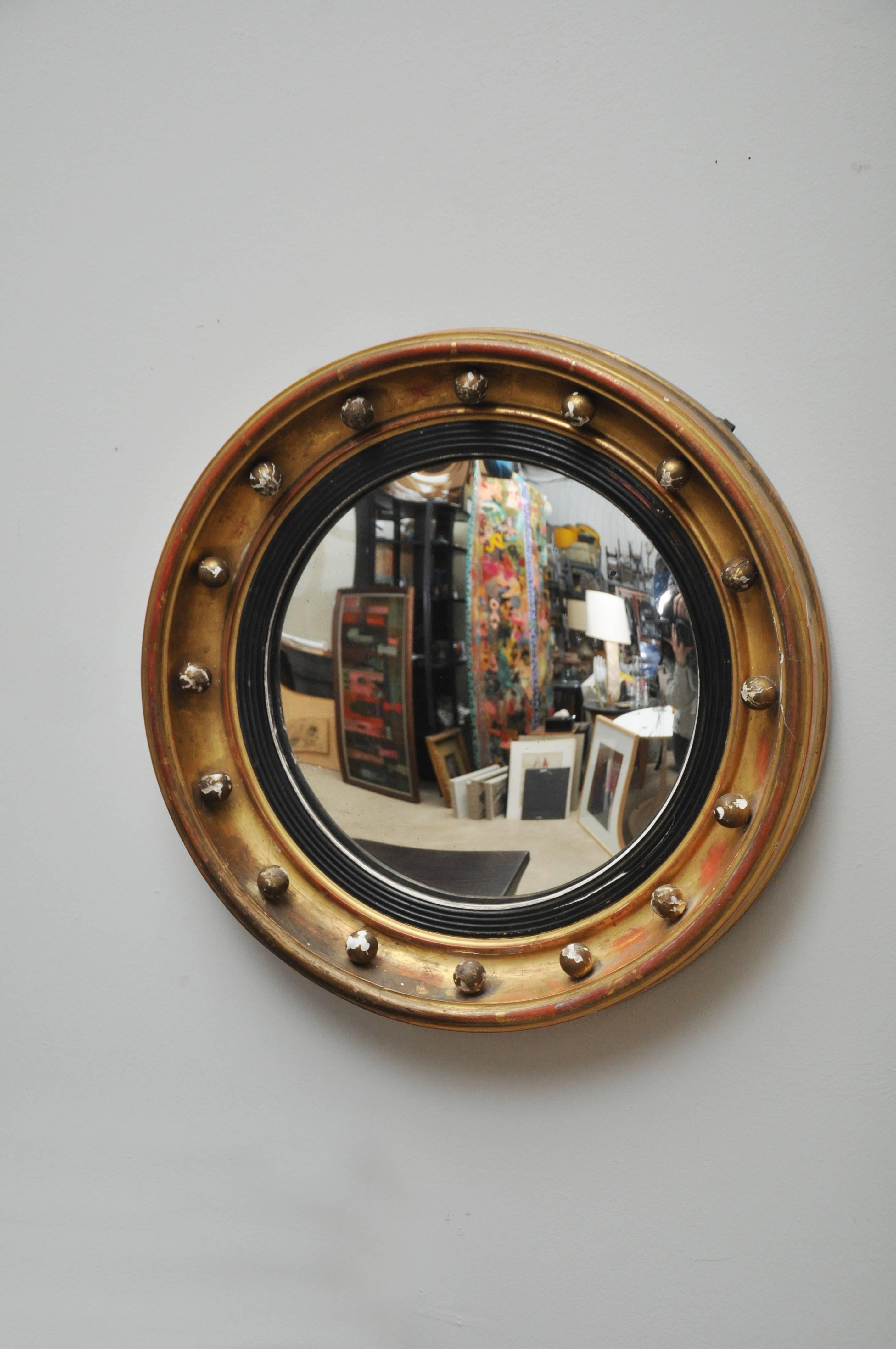 A circa 1930, Art Deco gold leaf convex bull's eye mirror from England. It is a Regency Georgian style mirror and has 16 decorative spheres around the frame along with an ebony surround and decorative geometric design. It retains the original 12