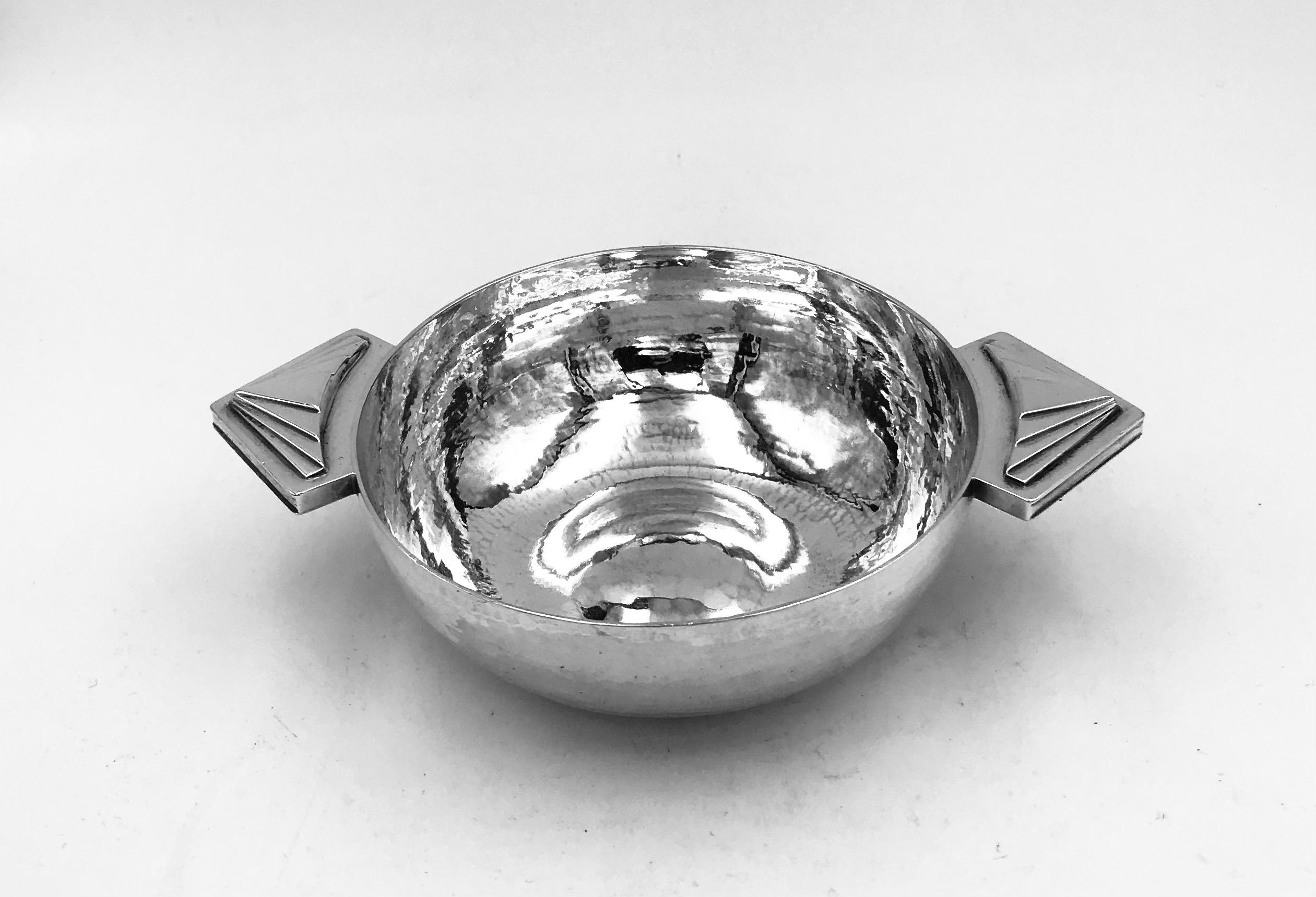 An Art Deco English silver bowl, hallmarked London 1932, designed by Robert Edgar Stone (1903-1990), and with his facsimile signature.
The diameter of the bowl is 10.5cm, and it measures 15.9cm across the handles