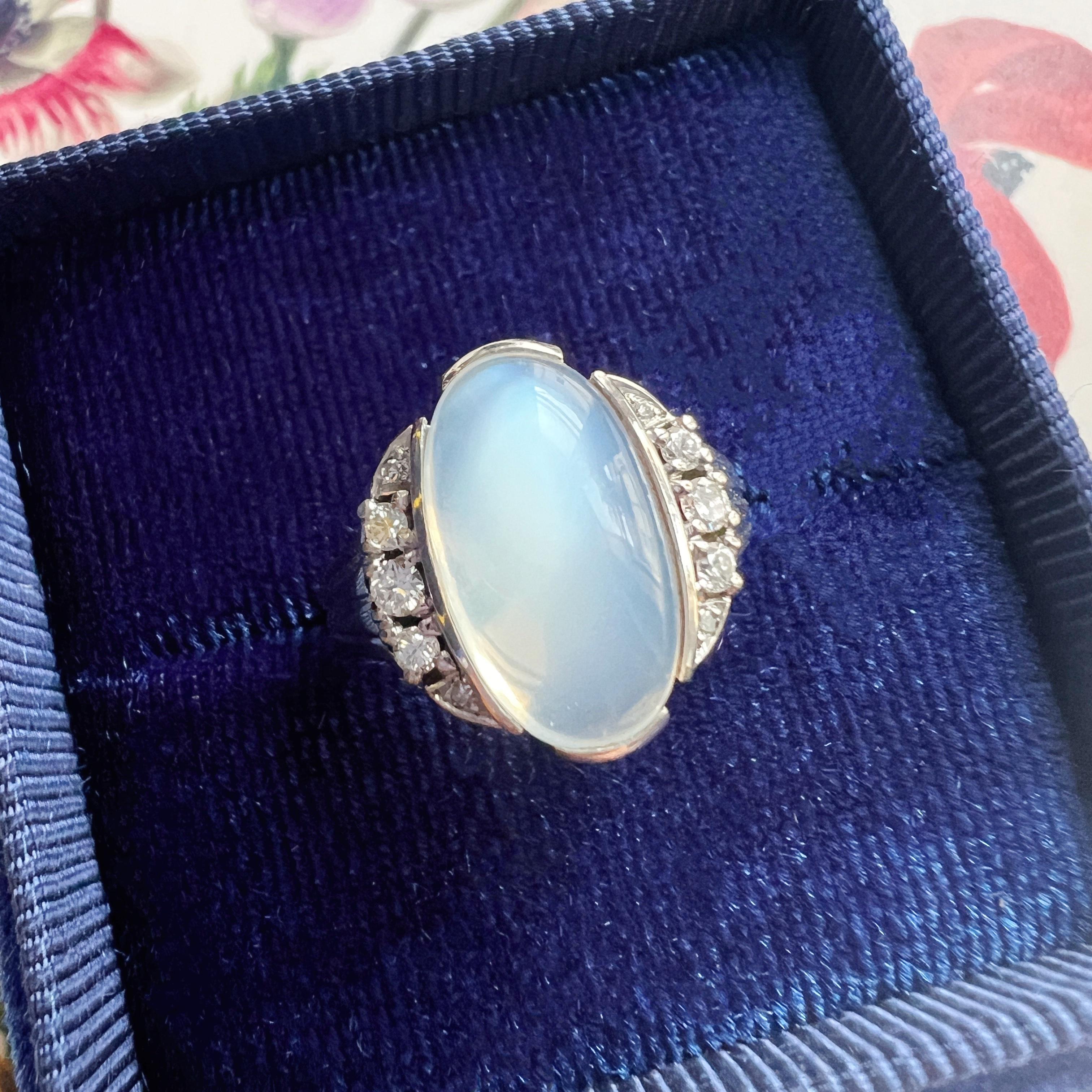 For sale an Art Deco era 18k white gold ring. At the heart of the ring is a large oval-shaped moonstone, measuring 15mm by 9.5mm, radiating with the most desirable bluish sheen. This feldspar gemstone, often associated with mystique and enchantment,