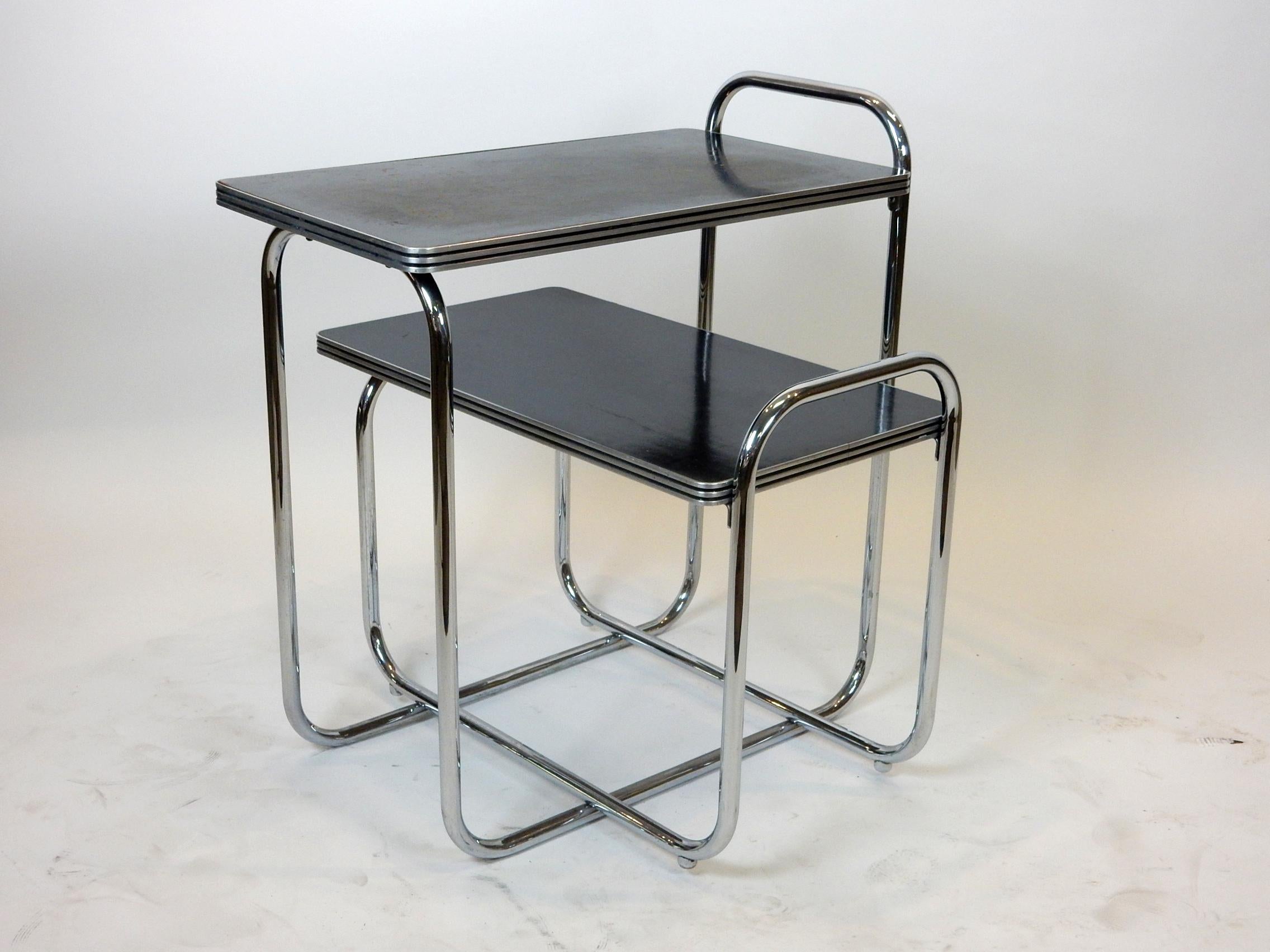 Seldom seen set manufactured by Troy Sunshade Co. designed by Gilbert Rohde.
Chromed steel tube with laminate wood tops.
Smaller table has protruding feet to keep it in place between the larger's rails.
They are 18 and 28 inches tall, both 28