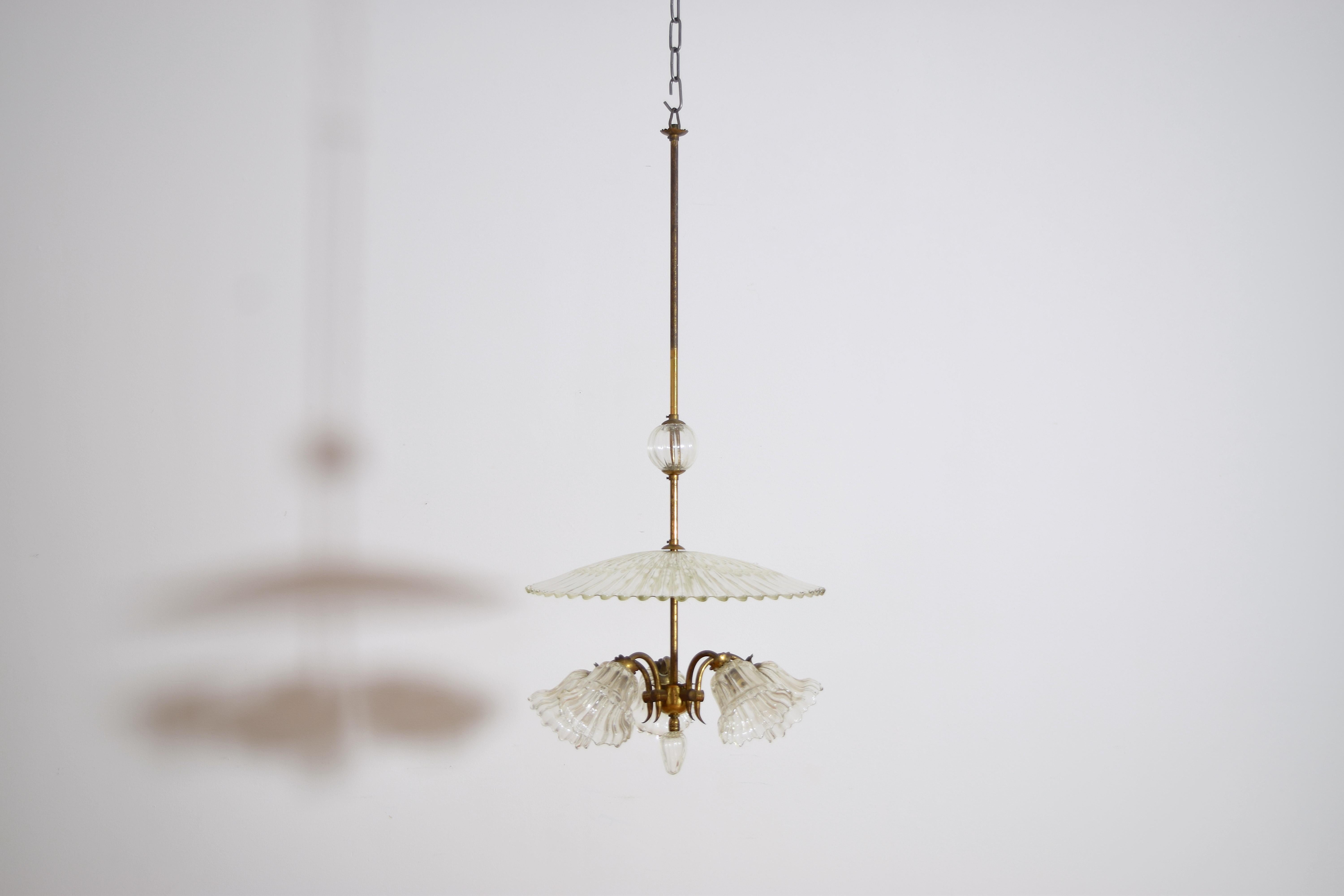 Un lustre Art déco en verre de Murano, réalisé par le designer Ercol Barovier, illustre le souci du détail et l'artisanat vénitiens des années 1930 ou 1940. 
Un abat-jour en forme de parasol en verre ondulé crée une ambiance unique. Les 5 récipients