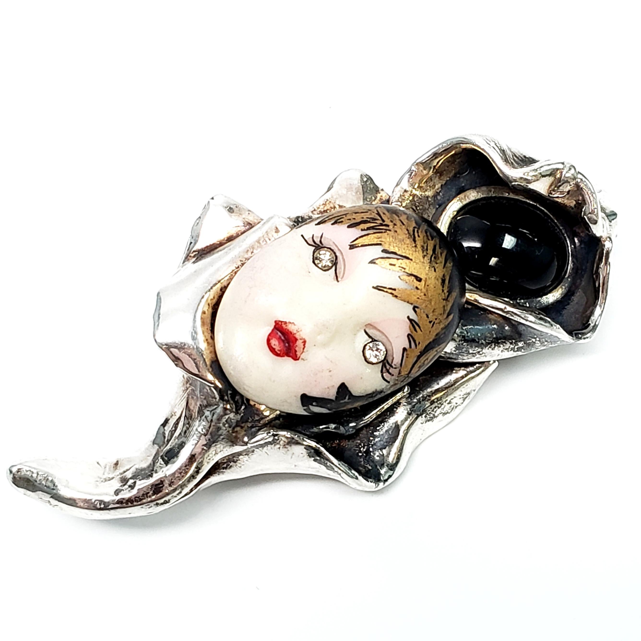 Sterling silver pin featuring an oval onyx stone and porcelain face by Eros.

This beautiful pin features a lady's painted face with crystal eyes, and an onyx bezel set in a sterling silver flower shaped pin.

Measures 1 3/8