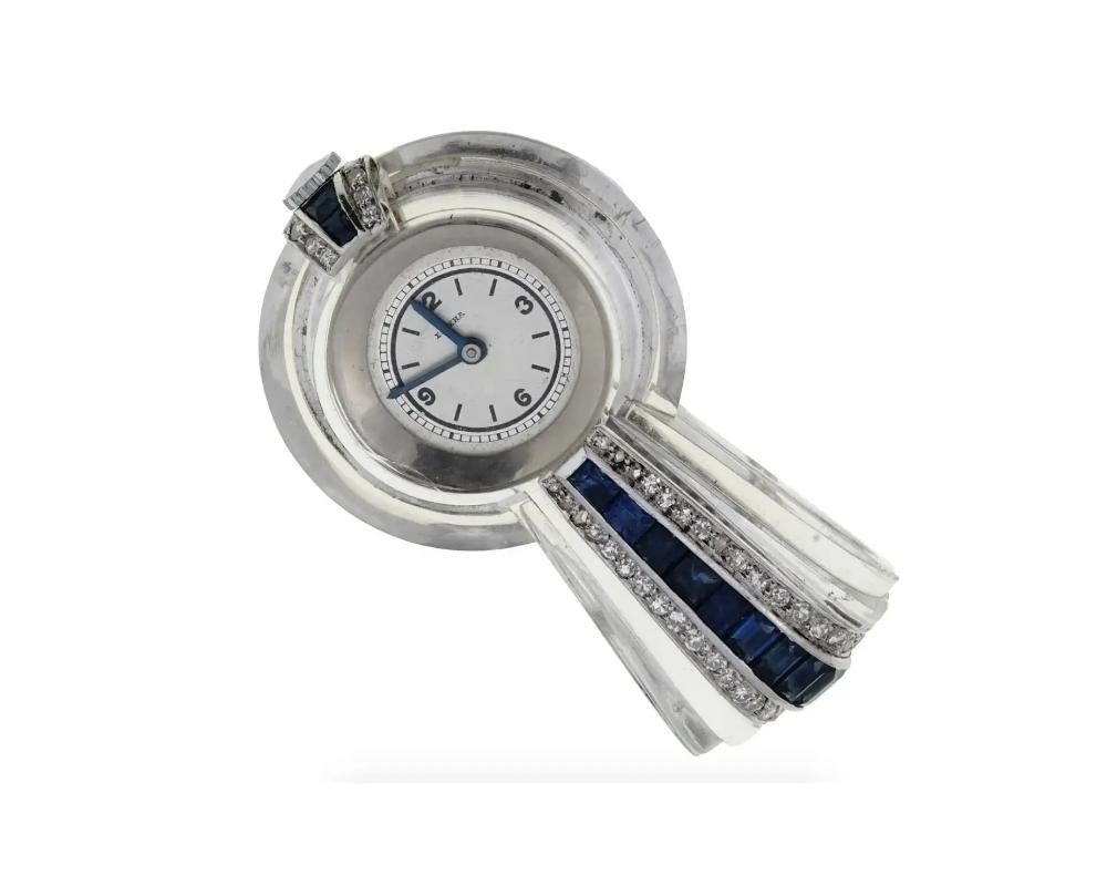 An antique Art Deco era lapel watch by Chopard, Boutique Special Editions Eszeha line. Clear glass and 14K white gold body garnished with faceted sapphires and diamons. White dial with Arabic and baton numerals, blue handles, marked Eszeha.