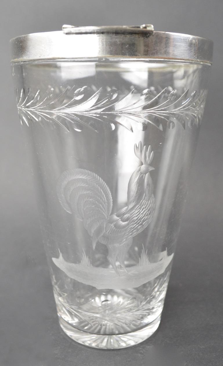 Stylish Art Deco Cocktail mixer with silver plate top rim. Rim shows minor wear to plating, as shown. Glass body has an etched Rooster, and wreath decoration. This cocktail will add class and sophistication to all your festive occasions.