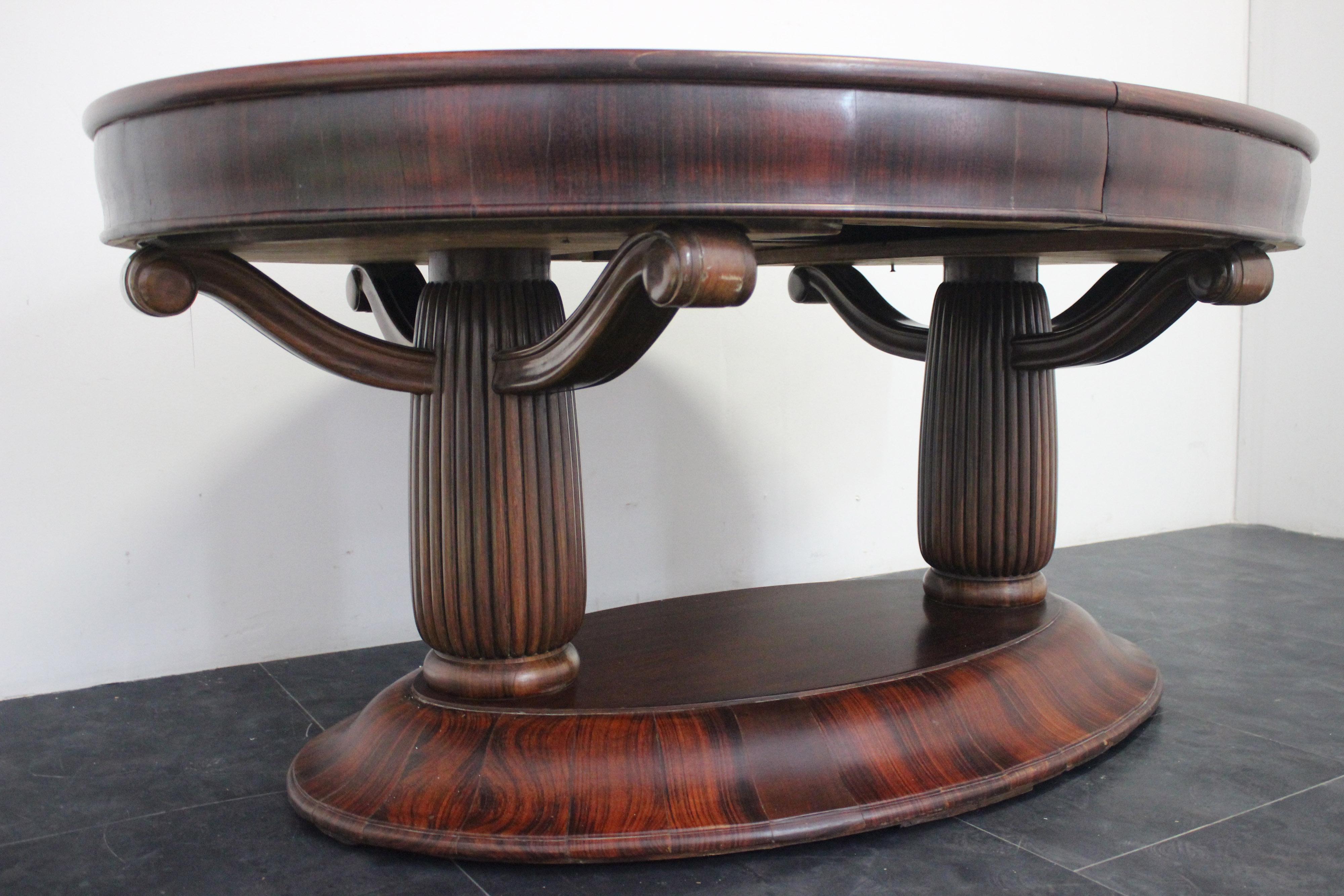 Imposanter ovaler Art-déco-Tisch aus massivem Palisanderholz. Der Sockel ist geformt und mit geflammten Teilen aus massivem Palisanderholz verkleidet, die ovalen Säulen sind gerillt, wobei drei Arme den Deckel tragen, wie unten in Fragmenten aus