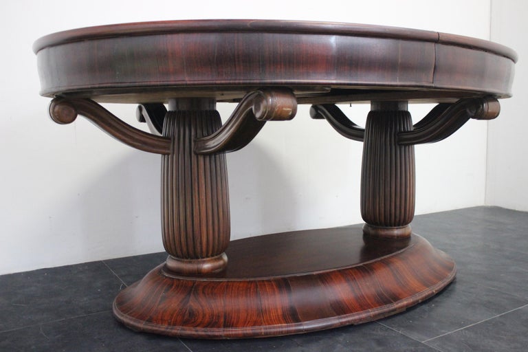 Imposing oval Art deco table in solid rosewood. The base is shaped and covered in flamed portions in solid rosewood, the oval columns are grooved, where three arms support the top, as below in fragments of flamed solid rosewood. The table can be