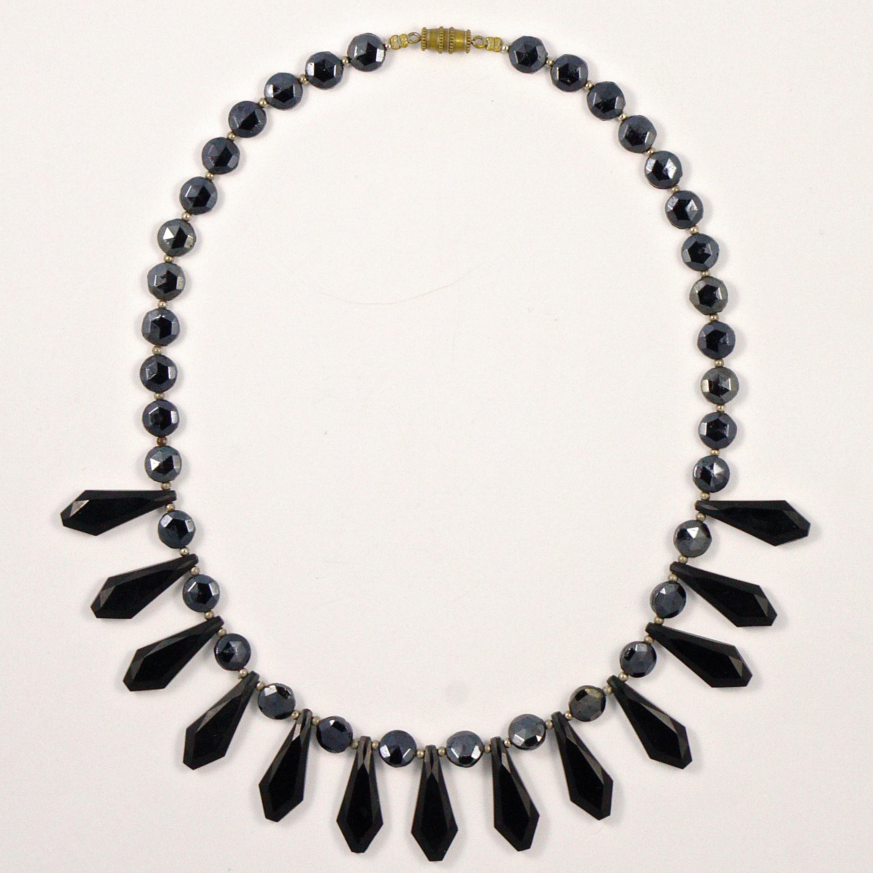 
Art Deco French jet fringe necklace, featuring faceted black glass drops and dark grey round beads, interspersed with small silver tone beads. The necklace closes with a barrel clasp. Measuring length 41cm / 16.1 inches, the drops are length 2.3cm