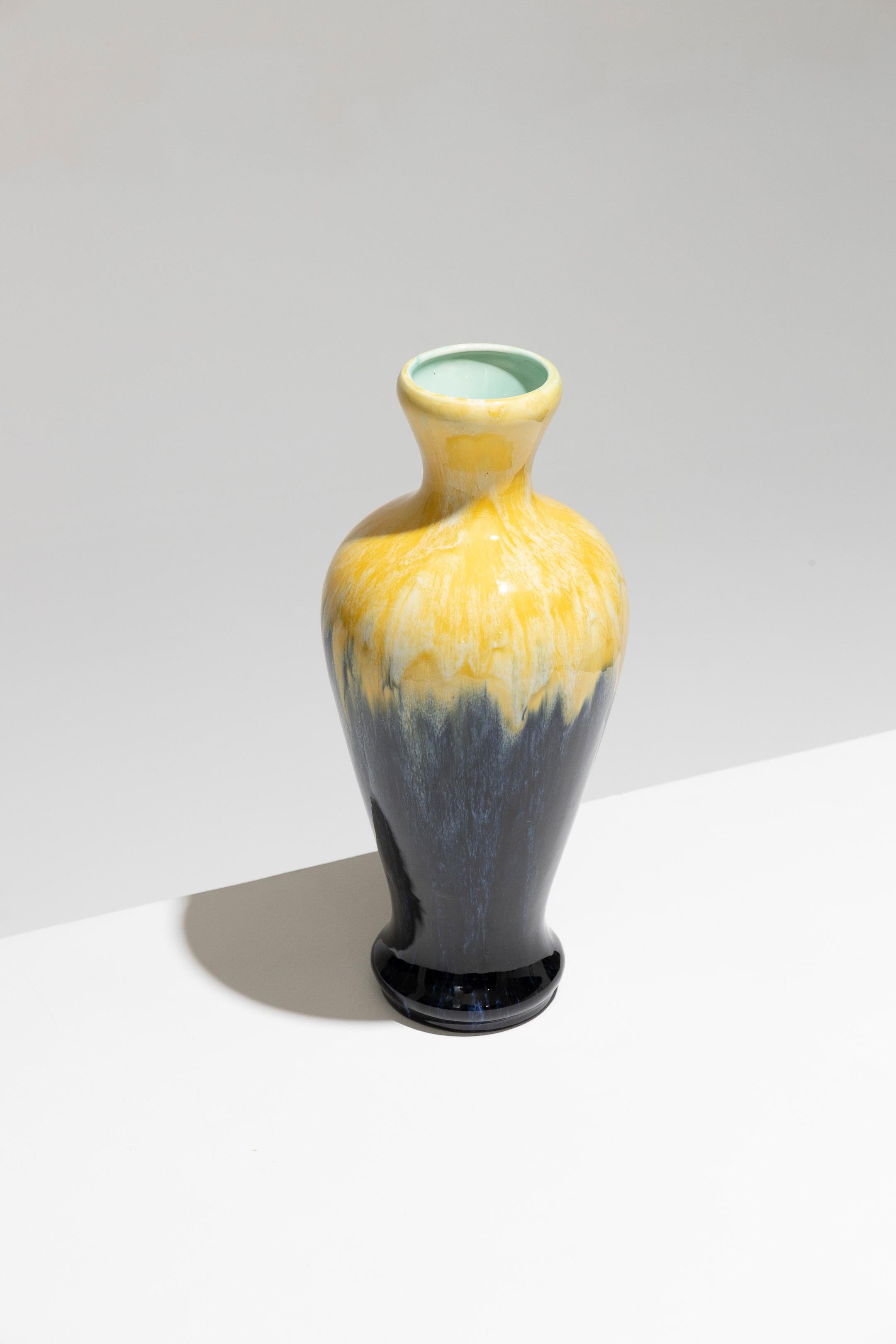 Vaso di maiolica con corpo oblungo su piedistallo, Manifattura Boch Frères Keramis, anni '30. Il vaso presenta un collo svasato ed è decorato con un disegno giallo fiammato fino alla spalla, seguito da una decorazione blu di tonalità marina sul