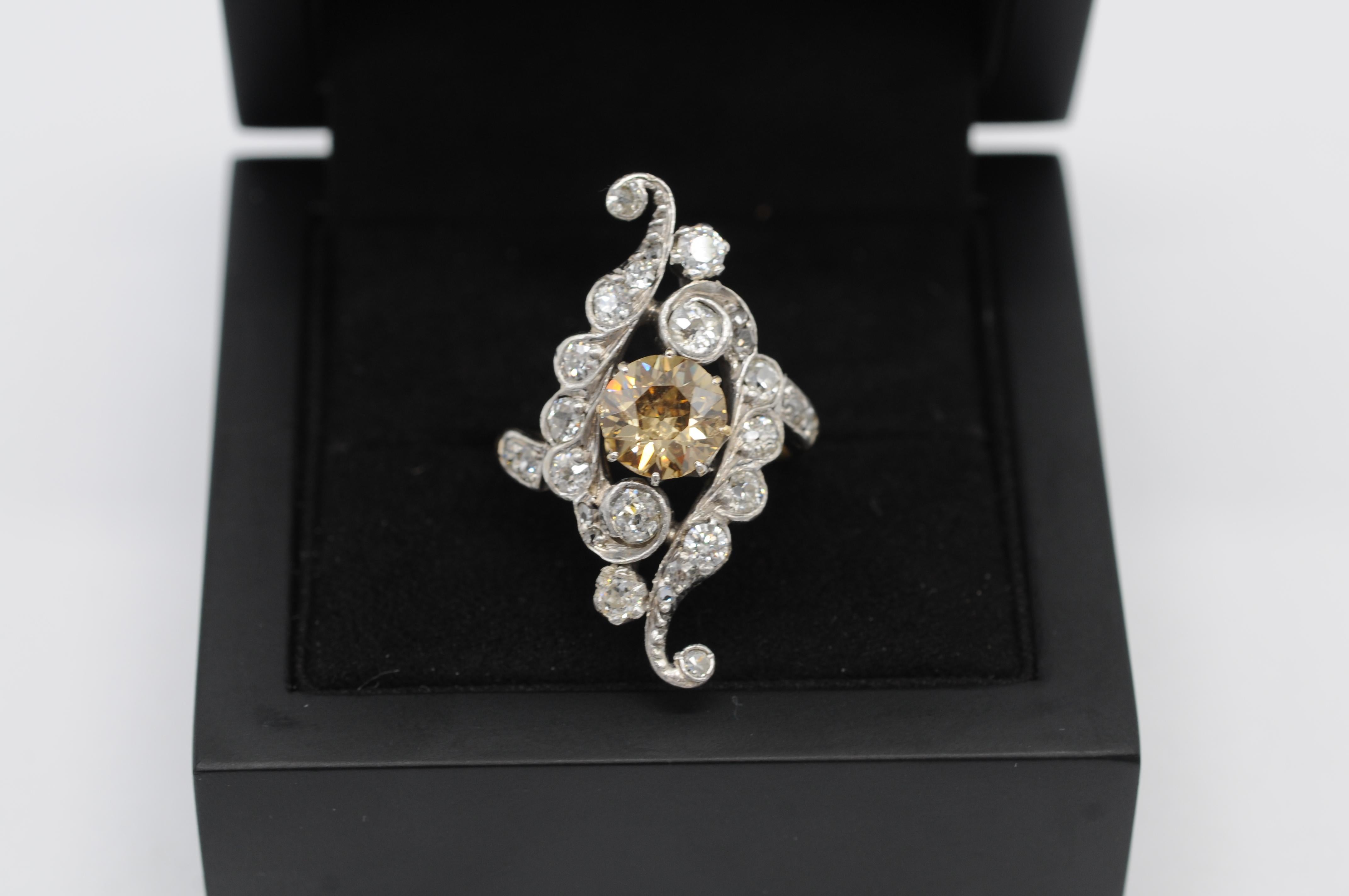 Erleben Sie die bezaubernde Anziehungskraft dieses Art-Déco-Clusterrings mit einem fesselnden braunen Fancy-Diamanten in einer Fassung aus 18 Karat Weiß- und Gelbgold. Dieses Schmuckstück vereint nahtlos Stil, Charme, Finesse und Schönheit und