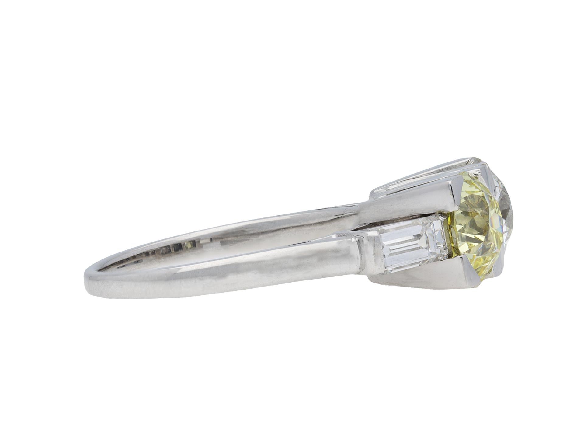 Art Deco fancy light yellow diamond two stone ring. Set with one round old cut fancy light yellow diamond, VS2 clarity with an approximate weight of 1.28 carats in an open back claw setting, further set with one round old cut diamond in an open back
