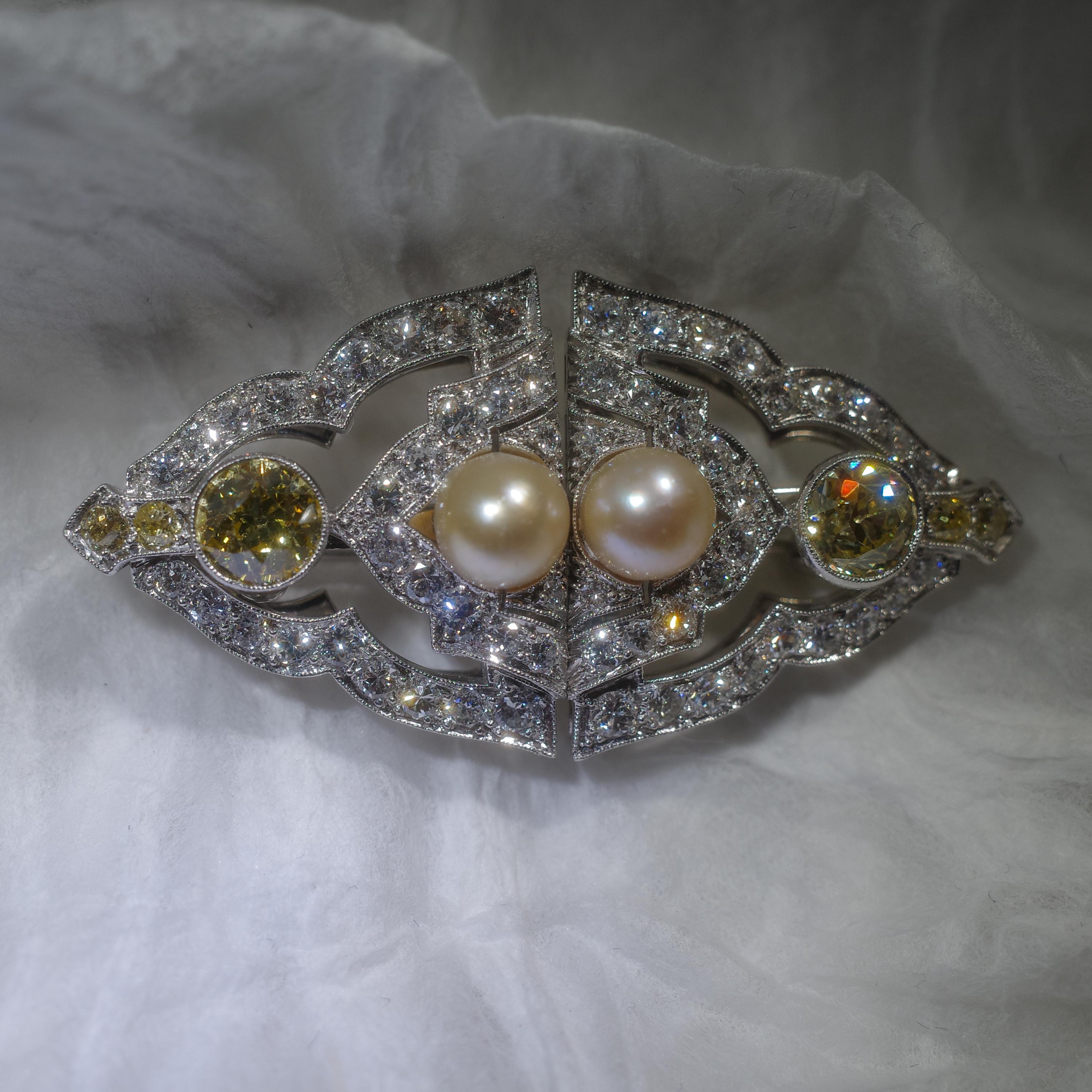 Esta pieza gloriosa y diabólicamente ingeniosa procede de la época Art Déco (hacia 1920). Se trata de un broche de platino reluciente que mide aproximadamente 42 mm de largo y 21 mm de ancho, y que lleva un par de perlas de agua salada naturales (no